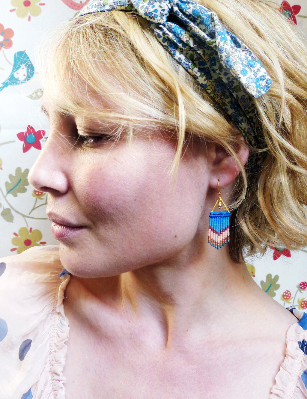 Peut inclure: Une femme aux cheveux blonds portant un bandeau floral et des boucles d'oreilles en perles bleues et roses. 