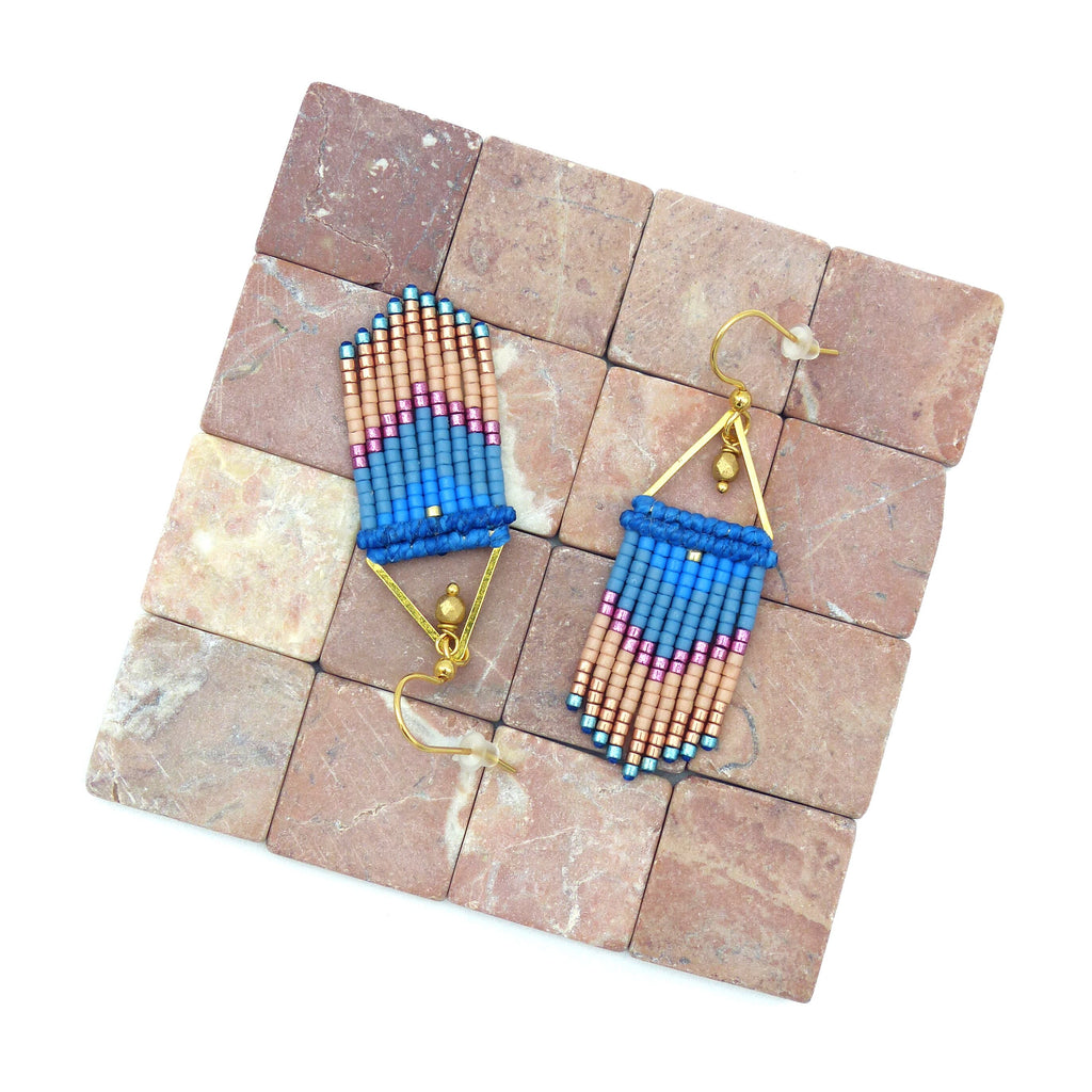 Peut inclure: Une paire de boucles d'oreilles dorées avec des franges de perles bleues, roses et pêche. Les boucles d'oreilles sont présentées sur une surface de carreaux bruns.