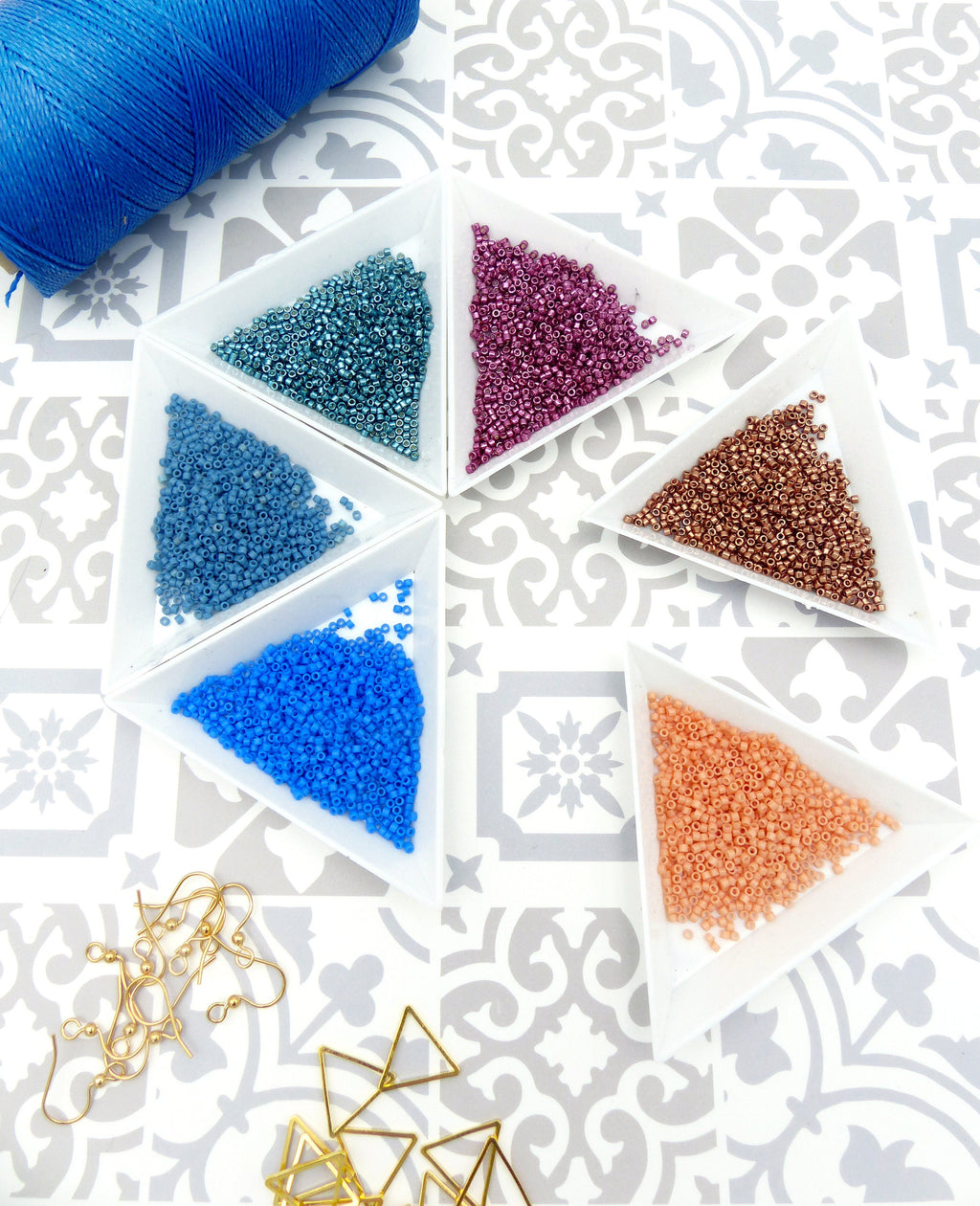 Peut inclure: Six petits plats triangulaires remplis de perles de rocaille de différentes couleurs. Les perles sont dans des tons de bleu, rose, cuivre et pêche. Il y a aussi des attaches de boucles d'oreilles dorées et des attaches de boucles d'oreilles en forme de triangle.