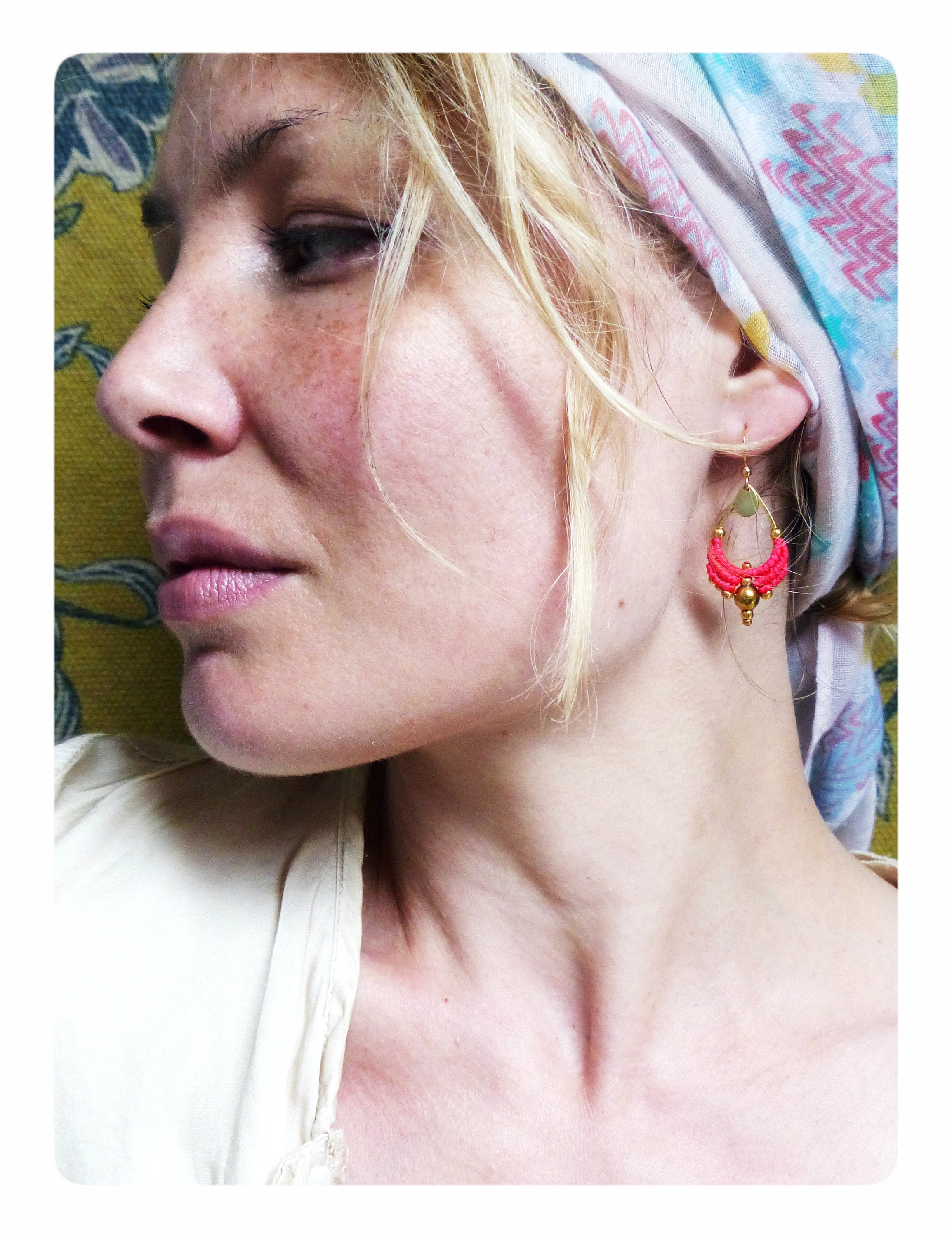 Peut inclure: Une femme aux cheveux blonds portant une chemise blanche et un foulard à motifs. Elle porte une paire de boucles d'oreilles pendantes roses et dorées.