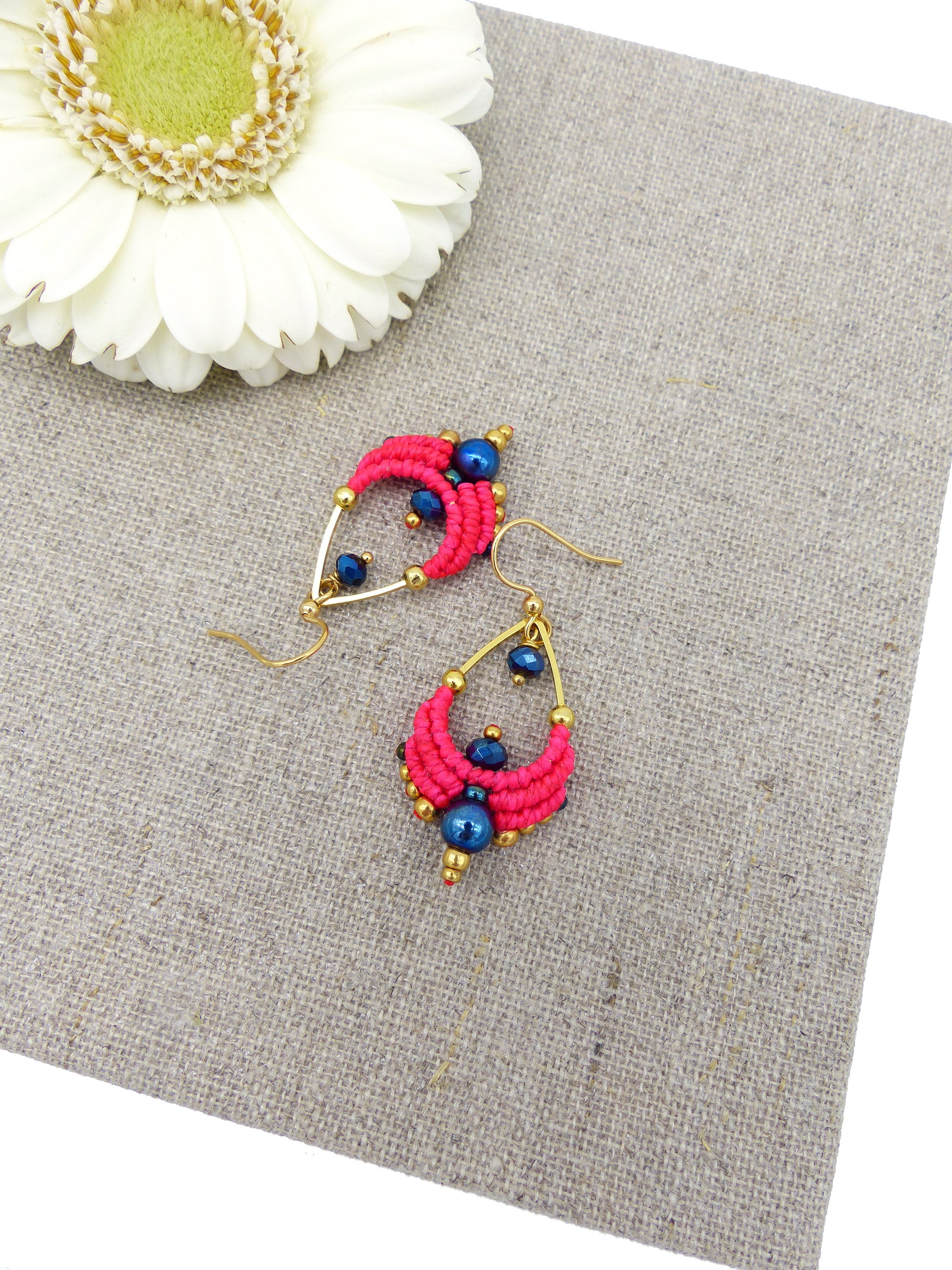 Peut inclure: Une paire de boucles d'oreilles rose et bleu avec des accents dorés. Les boucles d'oreilles sont faites de petites perles et ont une forme de larme.