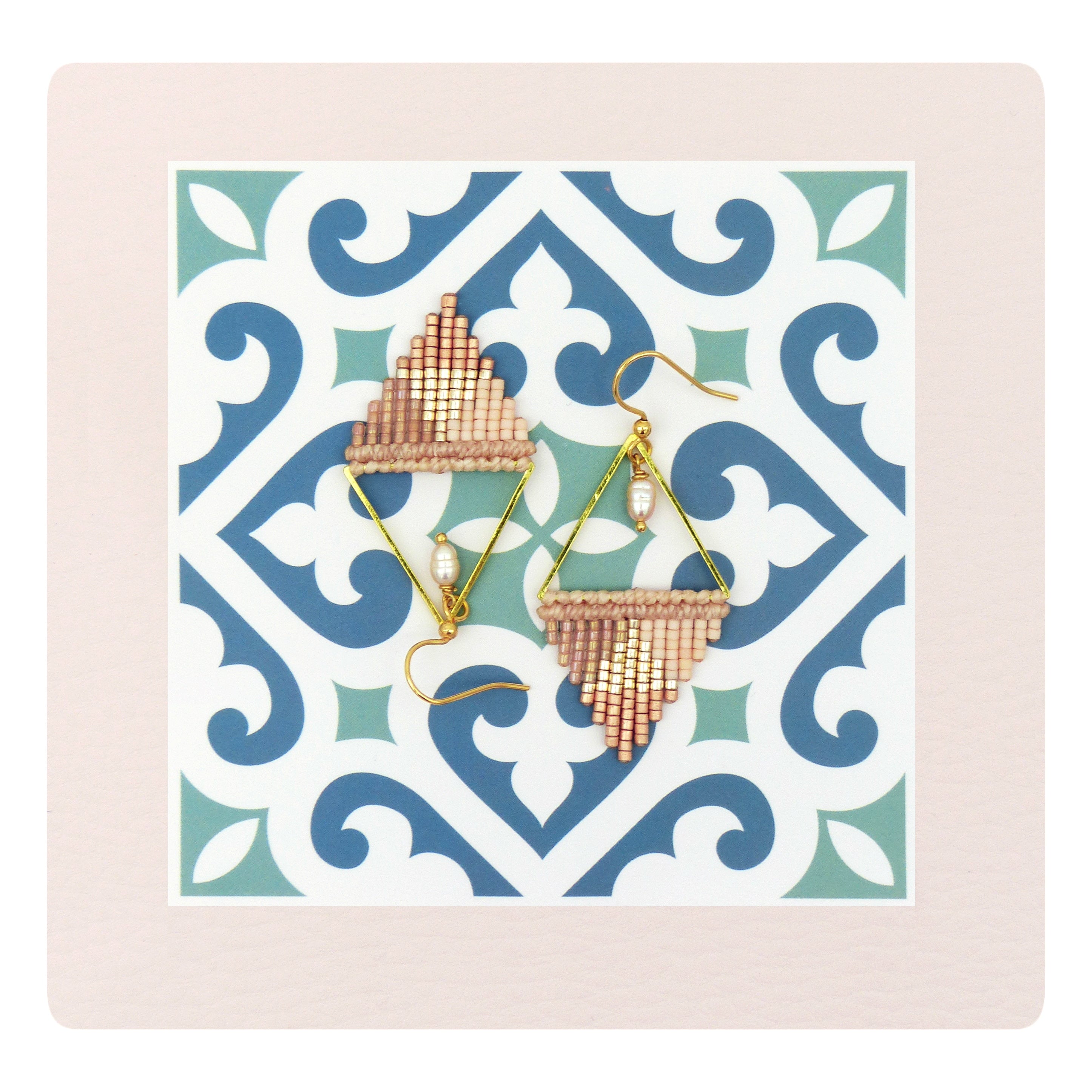 Peut inclure: Une paire de boucles d'oreilles triangulaires dorées avec une frange de perles rose et beige. Les boucles d'oreilles sont présentées sur un fond de carrelage à motifs.