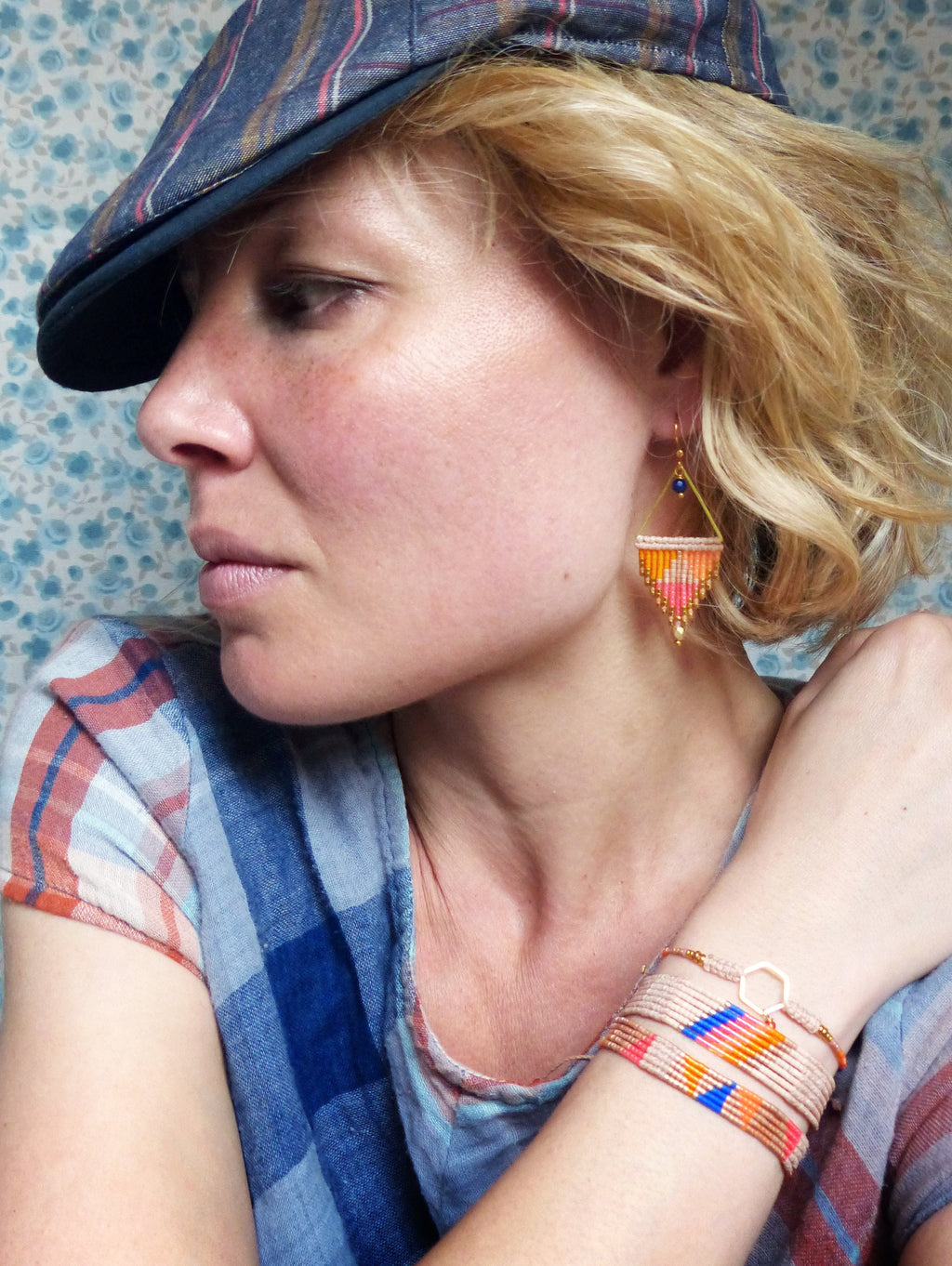 Peut inclure: Une femme portant une chemise à carreaux bleus et blancs avec une casquette plate et des boucles d'oreilles géométriques. Elle porte également plusieurs bracelets avec des perles colorées et un charme en or.