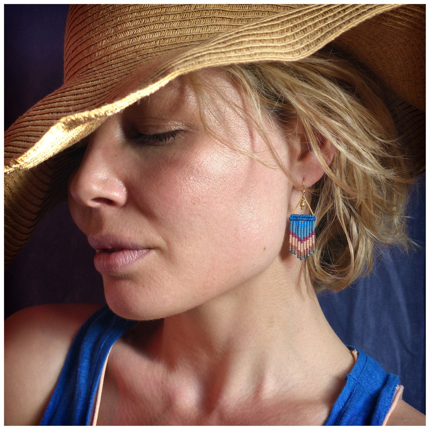 Peut inclure: Une femme portant un chapeau de paille à larges bords et un débardeur bleu. Elle porte des boucles d'oreilles en or avec des franges de perles bleues, roses et blanches.