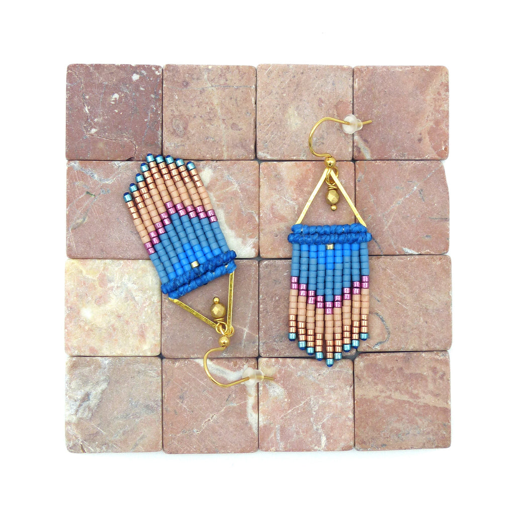 Peut inclure: Une paire de boucles d'oreilles pendantes avec un motif géométrique. Les boucles d'oreilles sont faites de perles bleues, roses et dorées. Les boucles d'oreilles sont suspendues à une surface carrelée.