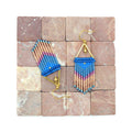 Peut inclure: Une paire de boucles d'oreilles pendantes avec un motif géométrique. Les boucles d'oreilles sont faites de perles bleues, roses et dorées. Les boucles d'oreilles sont suspendues à une surface carrelée.