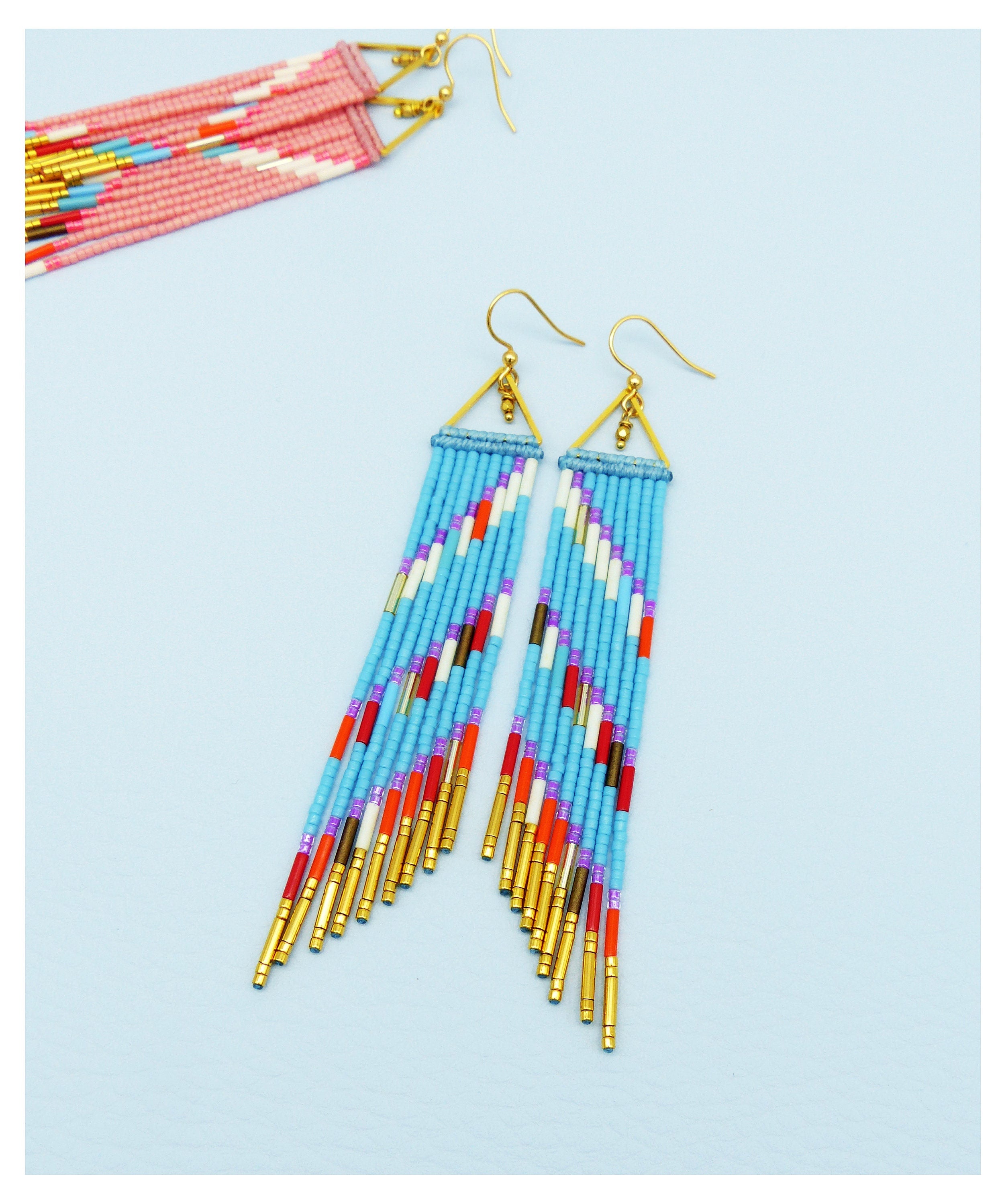 Peut inclure: Une paire de longues boucles d'oreilles en perles avec un motif géométrique. Les boucles d'oreilles sont faites de perles bleues, blanches, rouges, orange et violettes. Les boucles d'oreilles ont des accents dorés.