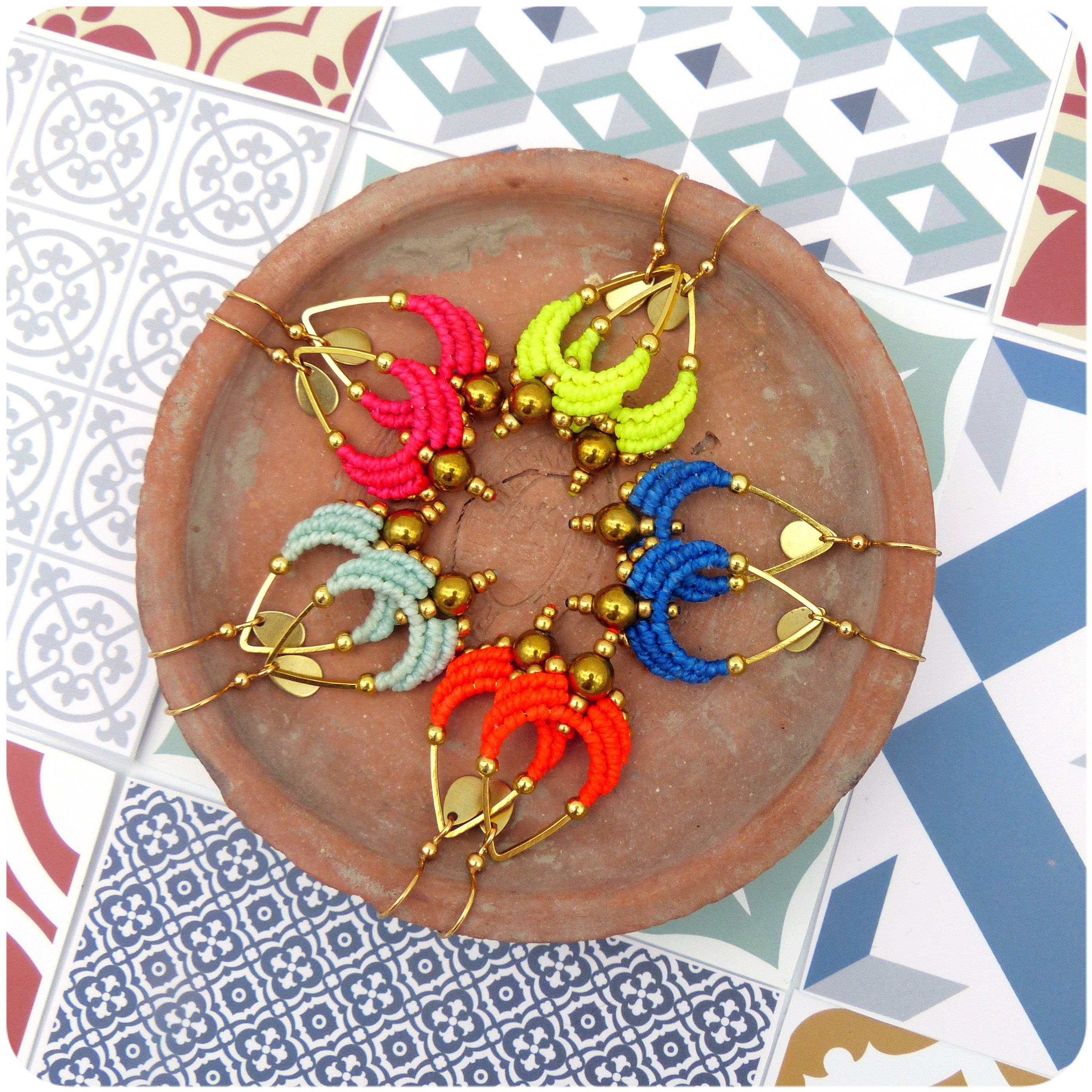 Peut inclure: Un ensemble de six boucles d'oreilles en perles colorées avec des anneaux dorés. Les boucles d'oreilles sont disposées en cercle sur une assiette en terre cuite.