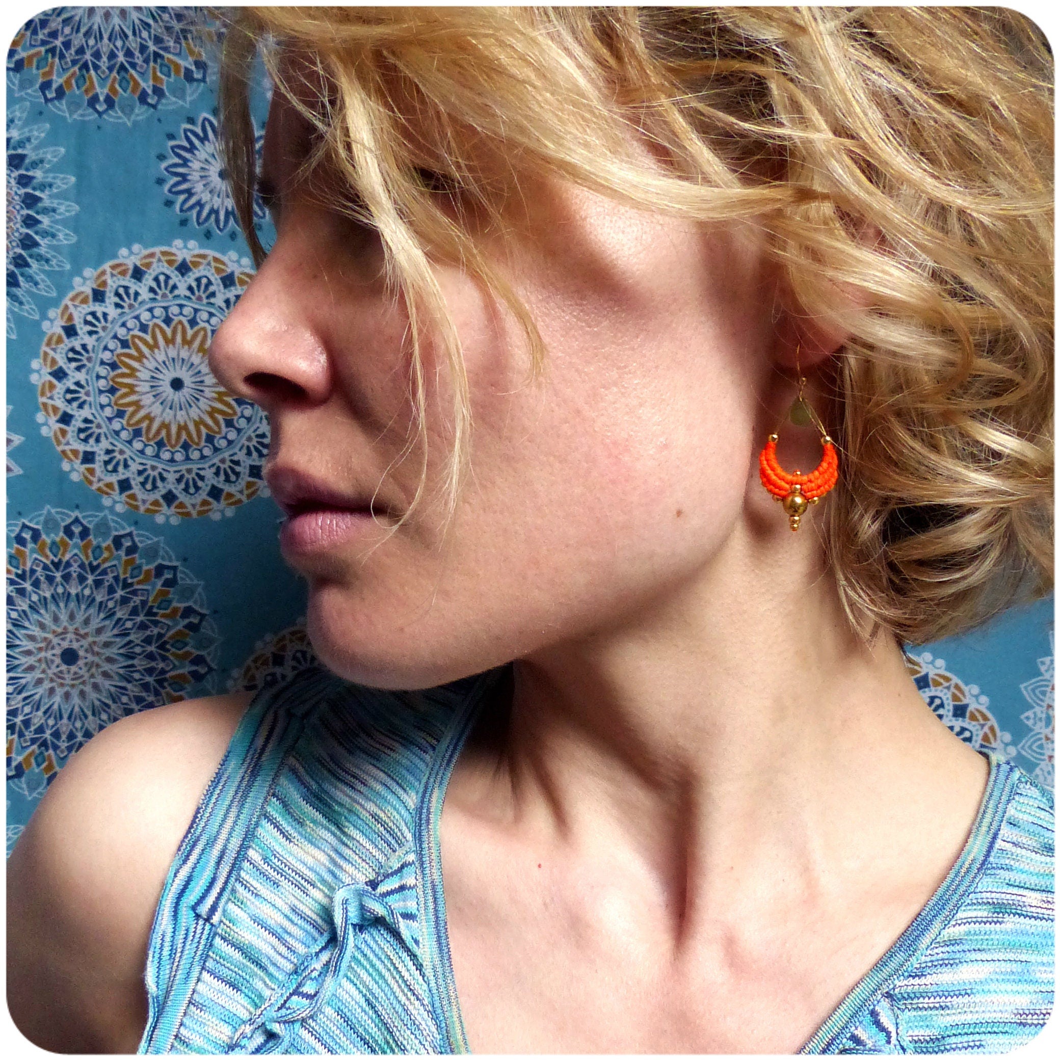 Peut inclure: Une femme portant une chemise rayée bleu et blanc avec des boucles d'oreilles orange et dorées. Les boucles d'oreilles sont en forme de croissant de lune.