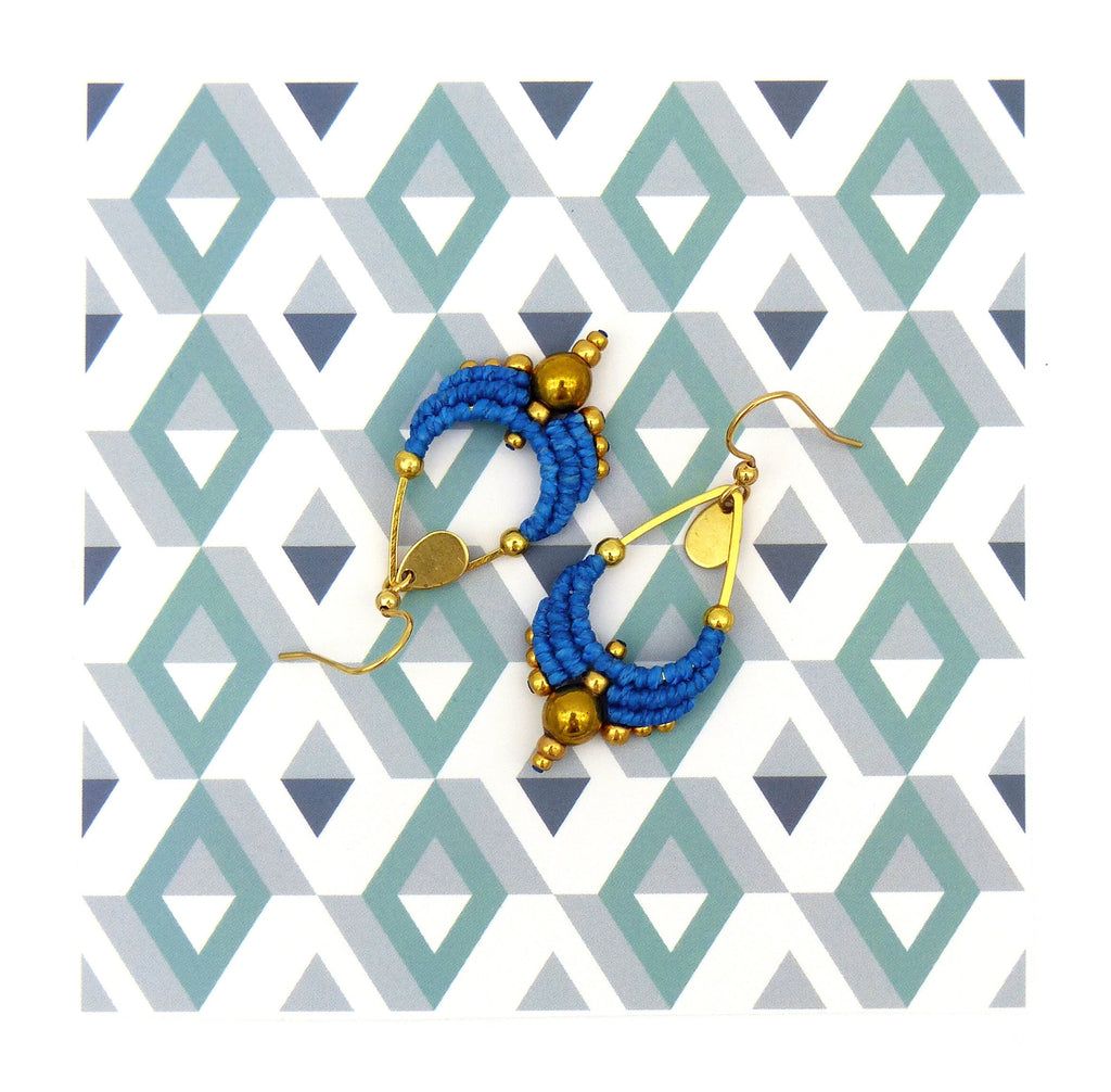 Peut inclure: Une paire de boucles d'oreilles en forme de goutte d'eau, de couleur bleue et dorée. Les boucles d'oreilles sont faites de fil tissé et ont une perle dorée au bas.