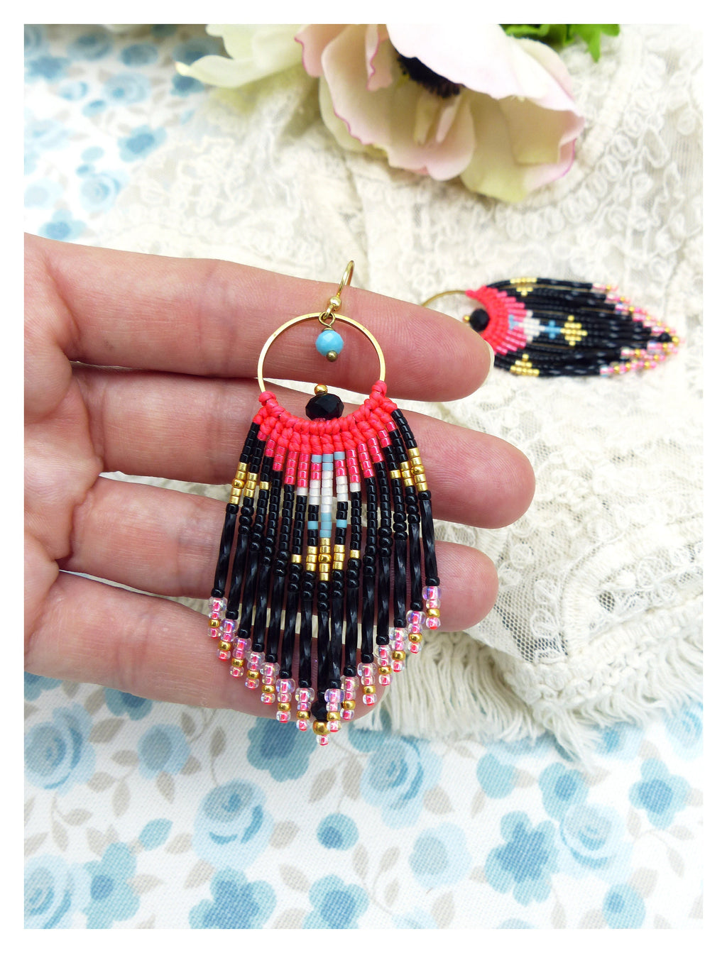 Peut inclure: Une paire de boucles d'oreilles en perles noires, roses et dorées avec un design en frange. Les boucles d'oreilles sont suspendues à un anneau doré avec une perle noire au centre.