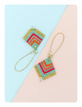 Peut inclure: Une paire de boucles d'oreilles en perles turquoise et dorées avec un motif géométrique. Les boucles d'oreilles sont sur un fond bleu clair et rose.