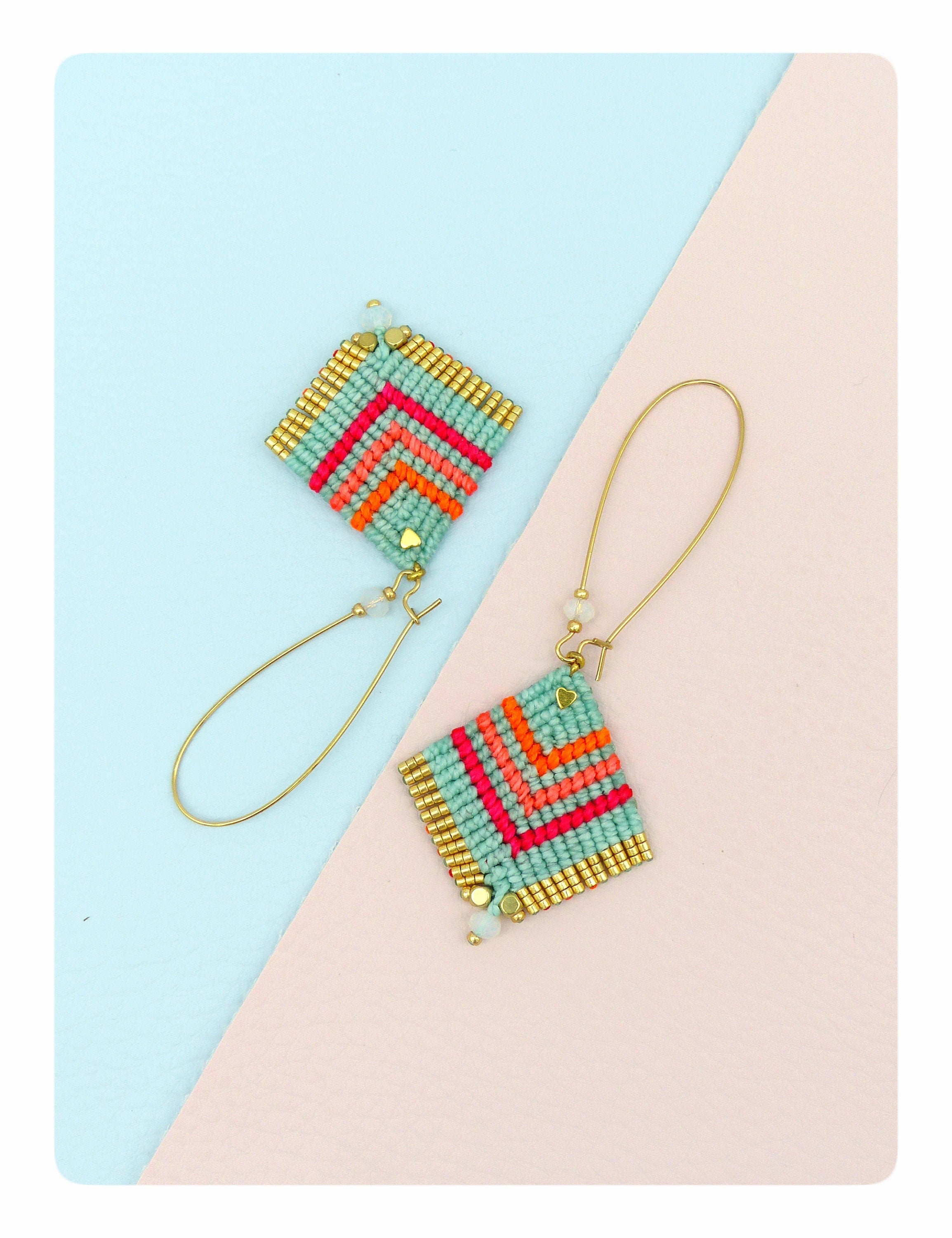 Peut inclure: Une paire de boucles d'oreilles en perles turquoise et dorées avec un motif géométrique. Les boucles d'oreilles sont sur un fond bleu clair et rose.