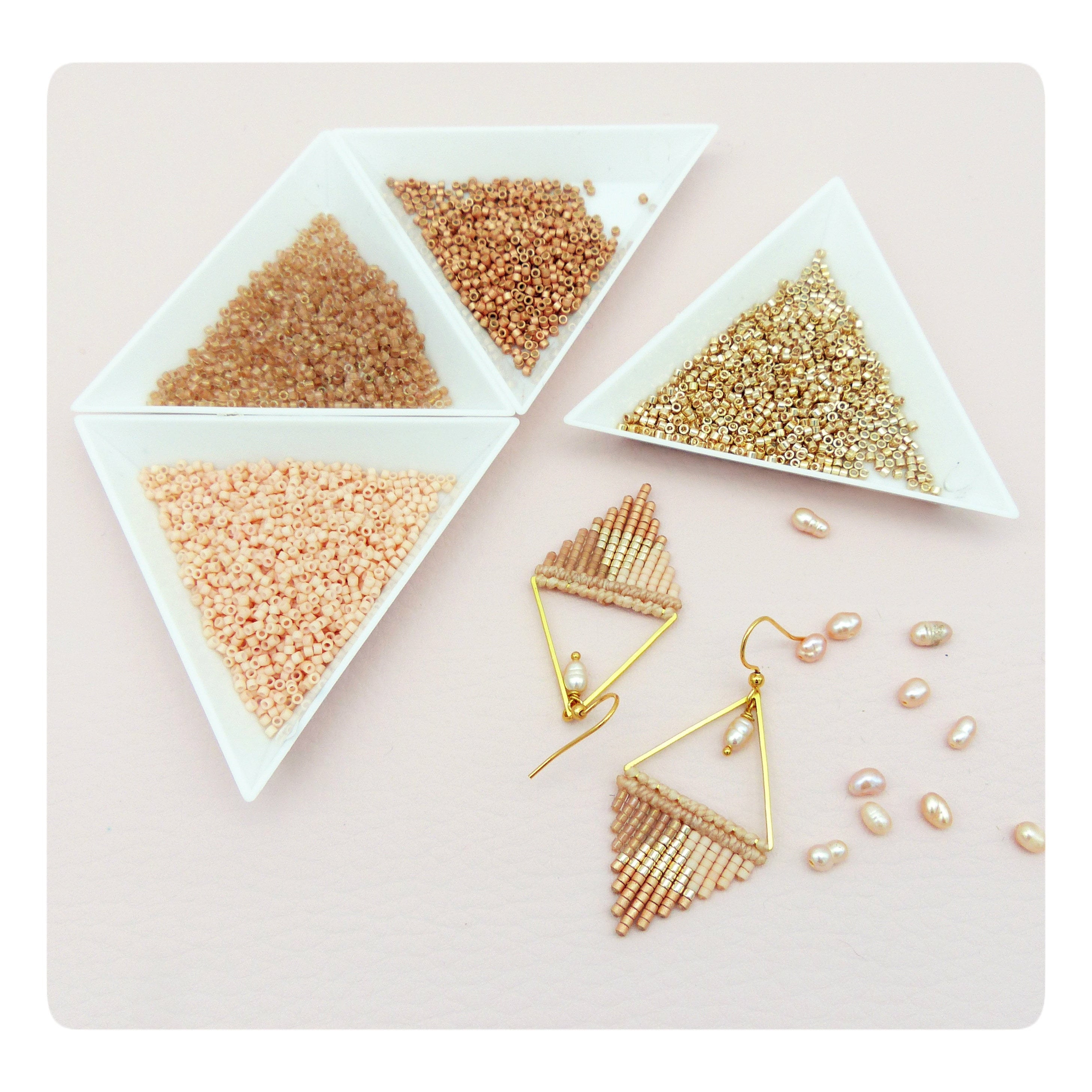 Peut inclure: Une paire de boucles d'oreilles triangulaires dorées avec des perles pêche et dorées. Les boucles d'oreilles sont présentées sur une surface rose avec de petites perles blanches et trois bols de perles en pêche, or et brun.