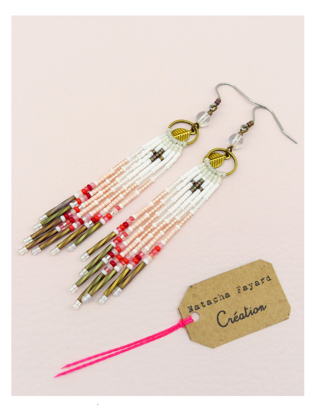 Peut inclure: Paire de boucles d'oreilles pendantes en perles, blanches, roses, rouges et bronze. Les boucles d'oreilles présentent un motif de croix et des breloques en forme de feuilles dorées. Une étiquette indique "Natacha Fayard Création".