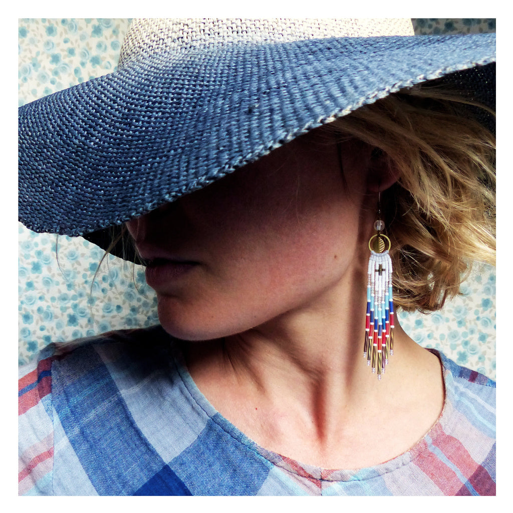 Peut inclure: Une femme portant une chemise à rayures bleues et blanches et un chapeau bleu et blanc à larges bords. Elle porte de longues boucles d'oreilles en perles avec des accents rouge, blanc et bleu.