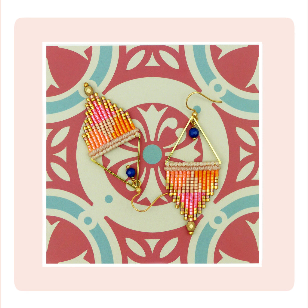 Peut inclure: Une paire de boucles d'oreilles triangulaires dorées avec une frange de perles roses, orange et blanches. Les boucles d'oreilles ont une perle bleue en haut.