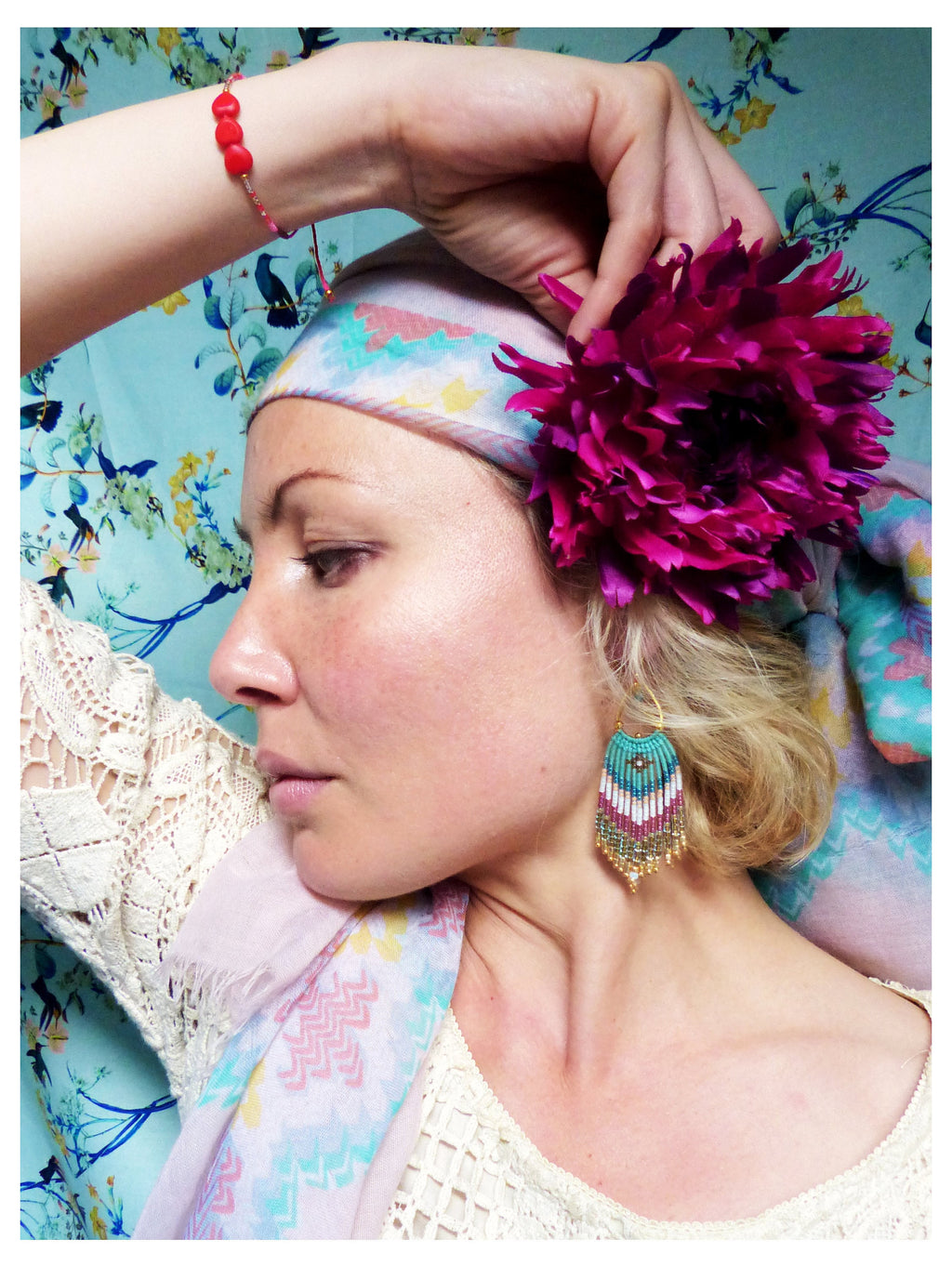 Peut inclure: Une femme portant un foulard à motifs roses et bleus avec une grande fleur rose sur le dessus. Elle porte un haut en crochet blanc et des boucles d'oreilles en perles turquoise et dorées.