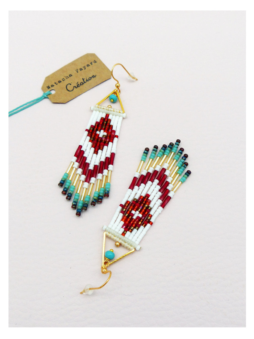 Peut inclure: Une paire de longues boucles d'oreilles en perles avec un sommet triangulaire et une perle turquoise. Les boucles d'oreilles sont faites de perles blanches, rouges et dorées.