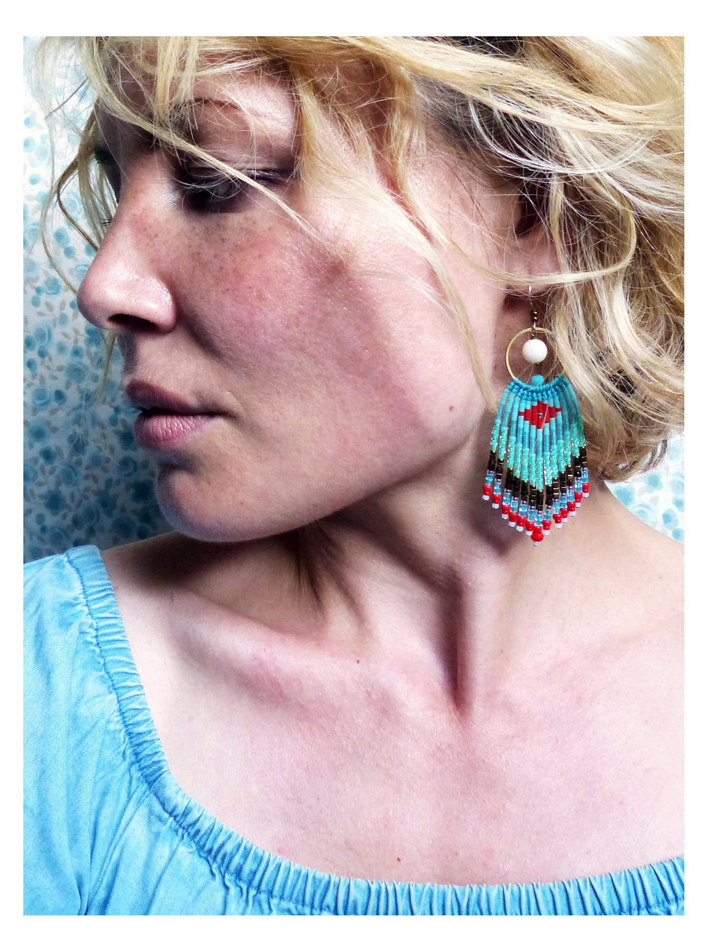Peut inclure: Une femme portant un haut bleu clair avec une paire de boucles d'oreilles en perles turquoise, rouge et blanc. Les boucles d'oreilles sont longues et pendent de ses oreilles.