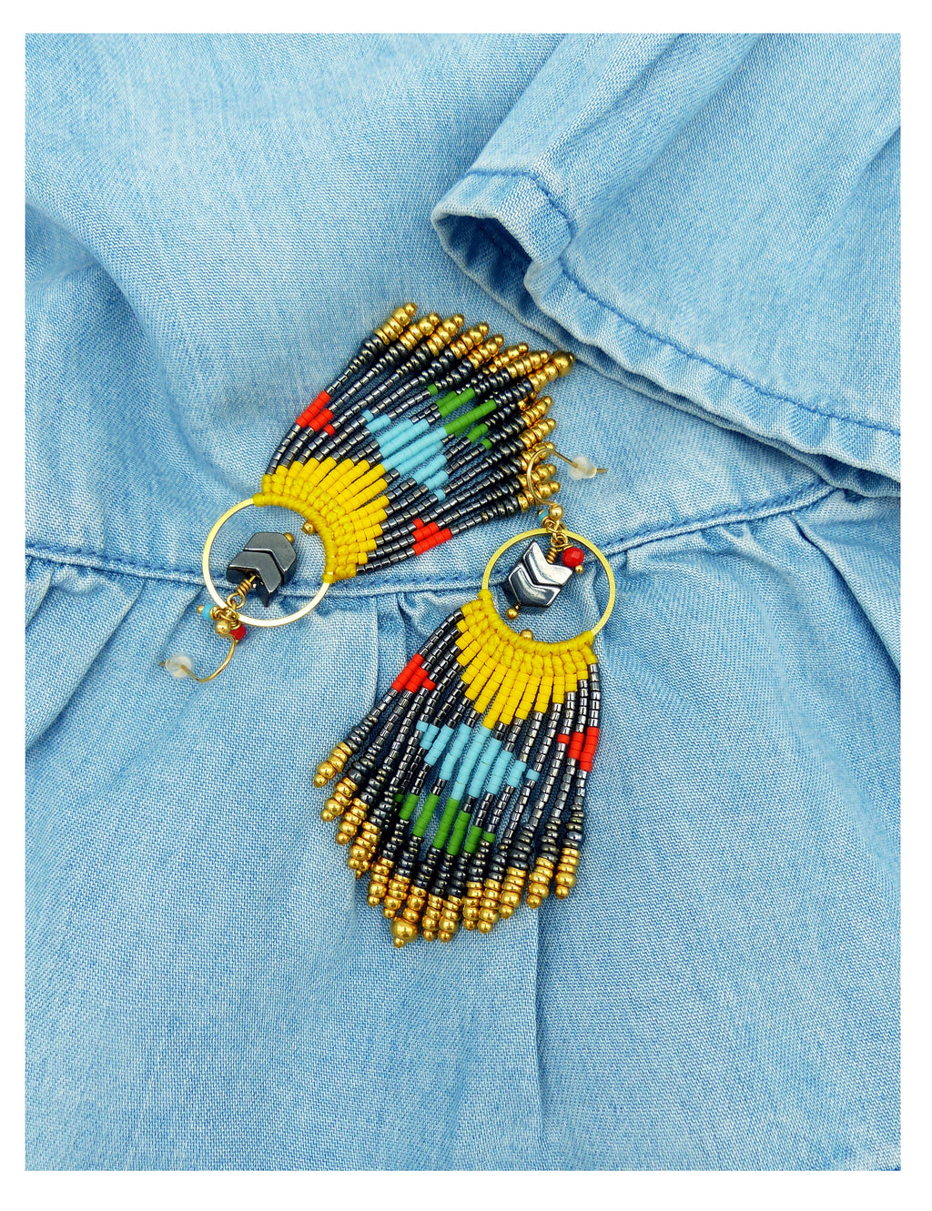 Peut inclure: Une paire de boucles d'oreilles en perles colorées avec un design en frange. Les boucles d'oreilles sont faites de perles jaunes, bleues, vertes, rouges et noires. Les boucles d'oreilles sont suspendues à des anneaux dorés.