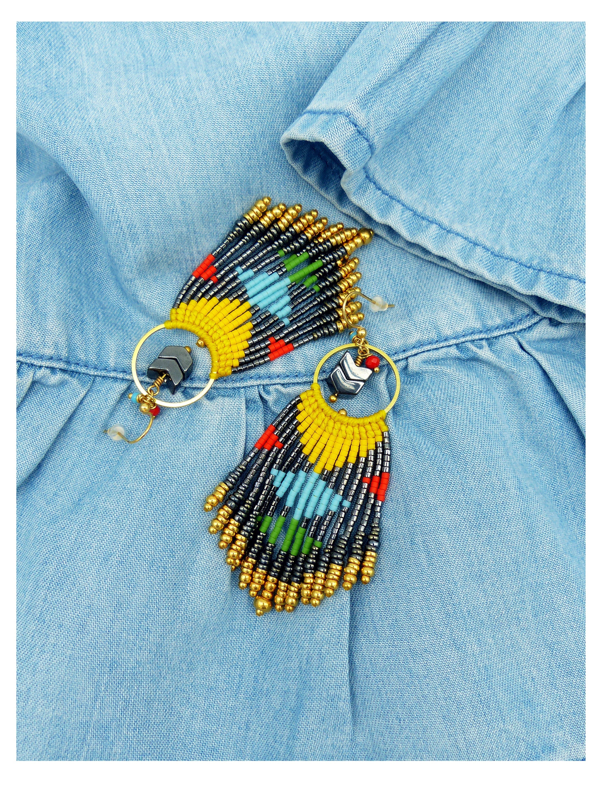 Peut inclure: Une paire de boucles d'oreilles en perles colorées avec un design en frange. Les boucles d'oreilles sont faites de perles jaunes, bleues, vertes, rouges et noires. Les boucles d'oreilles sont suspendues à des anneaux dorés.