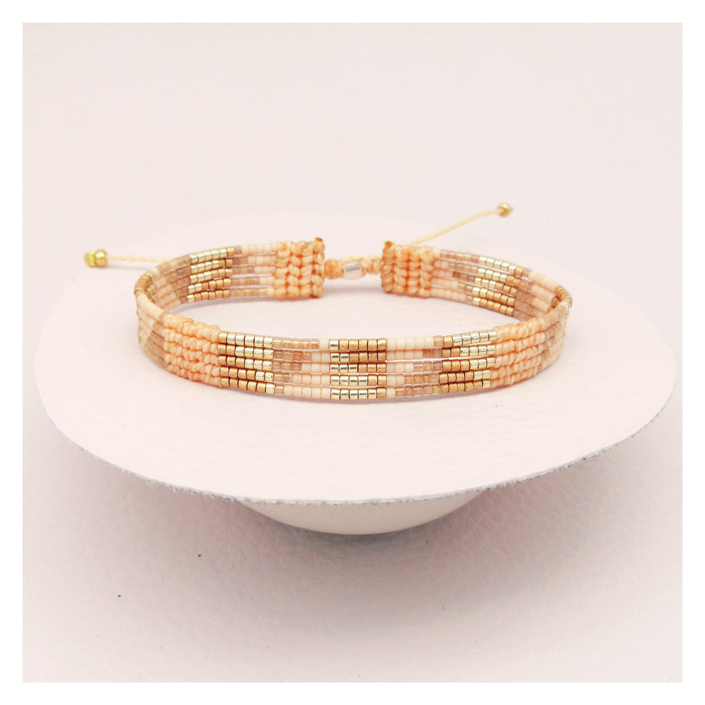 Peut inclure: Un bracelet délicat composé de petites perles colorées dans des tons de pêche, beige et or. Le bracelet est noué avec un cordon fin et possède un nœud coulissant pour ajuster la taille.
