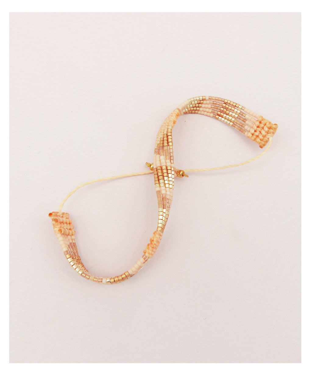 Peut inclure: Un bracelet délicat composé de petites perles multicolores dans des tons de pêche, blanc et or. Le bracelet est enfilé sur un cordon blanc fin.
