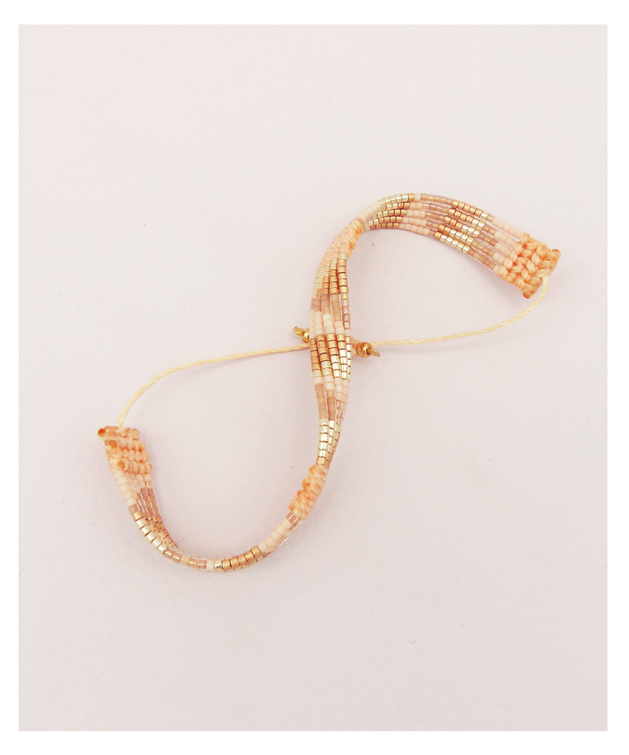 Peut inclure: Un bracelet délicat composé de petites perles multicolores dans des tons de pêche, blanc et or. Le bracelet est enfilé sur un cordon blanc fin.