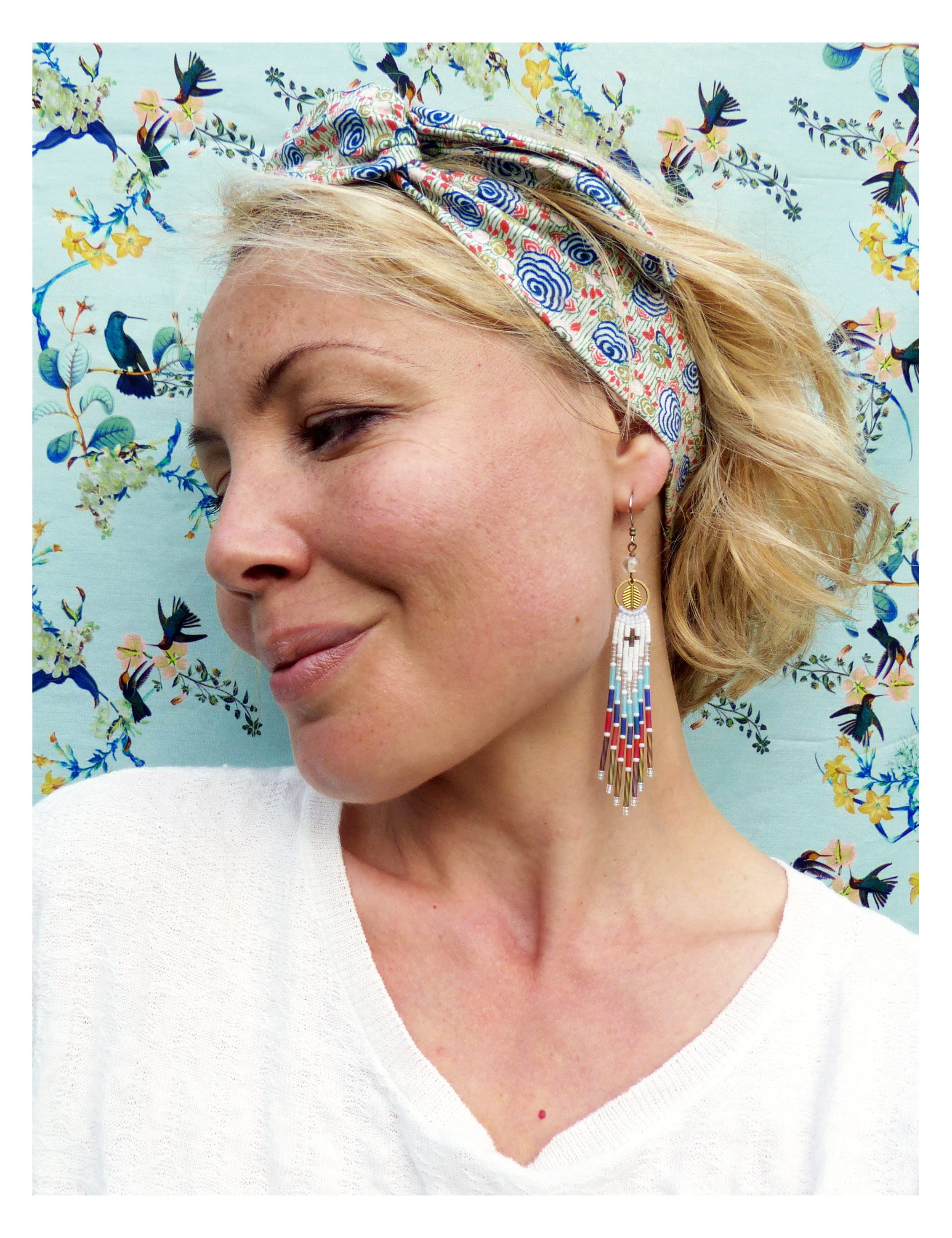 Peut inclure: Une femme portant une chemise blanche et un bandeau à motifs avec un nœud noué. Elle porte de longues boucles d'oreilles en perles avec un accent doré.