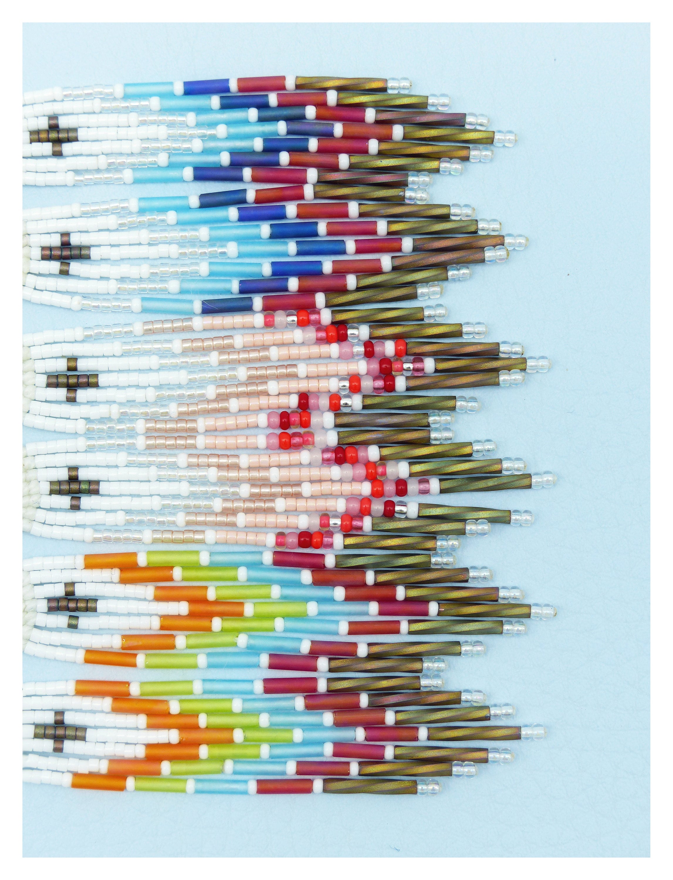 Peut inclure: Une frange de perles avec un motif arc-en-ciel. La frange est faite de petites perles colorées enfilées sur des fils fins. Les perles sont disposées selon un motif répétitif de blanc, orange, jaune, vert, bleu, rouge et rose.