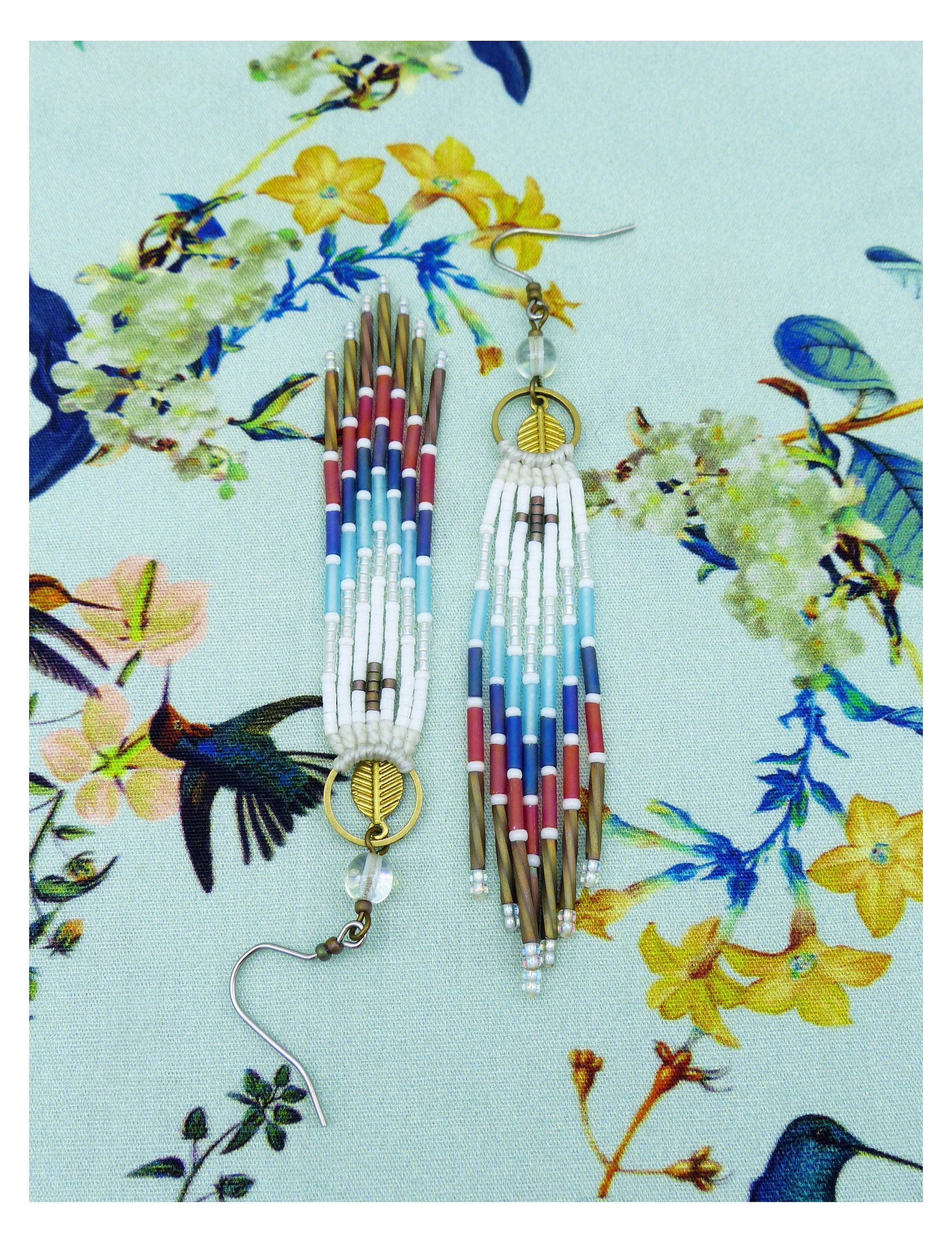 Peut inclure: Une paire de longues boucles d'oreilles en perles avec un motif de couleurs blanc, bleu et rouge. Les boucles d'oreilles ont un charme en forme de feuille dorée et un crochet argenté.