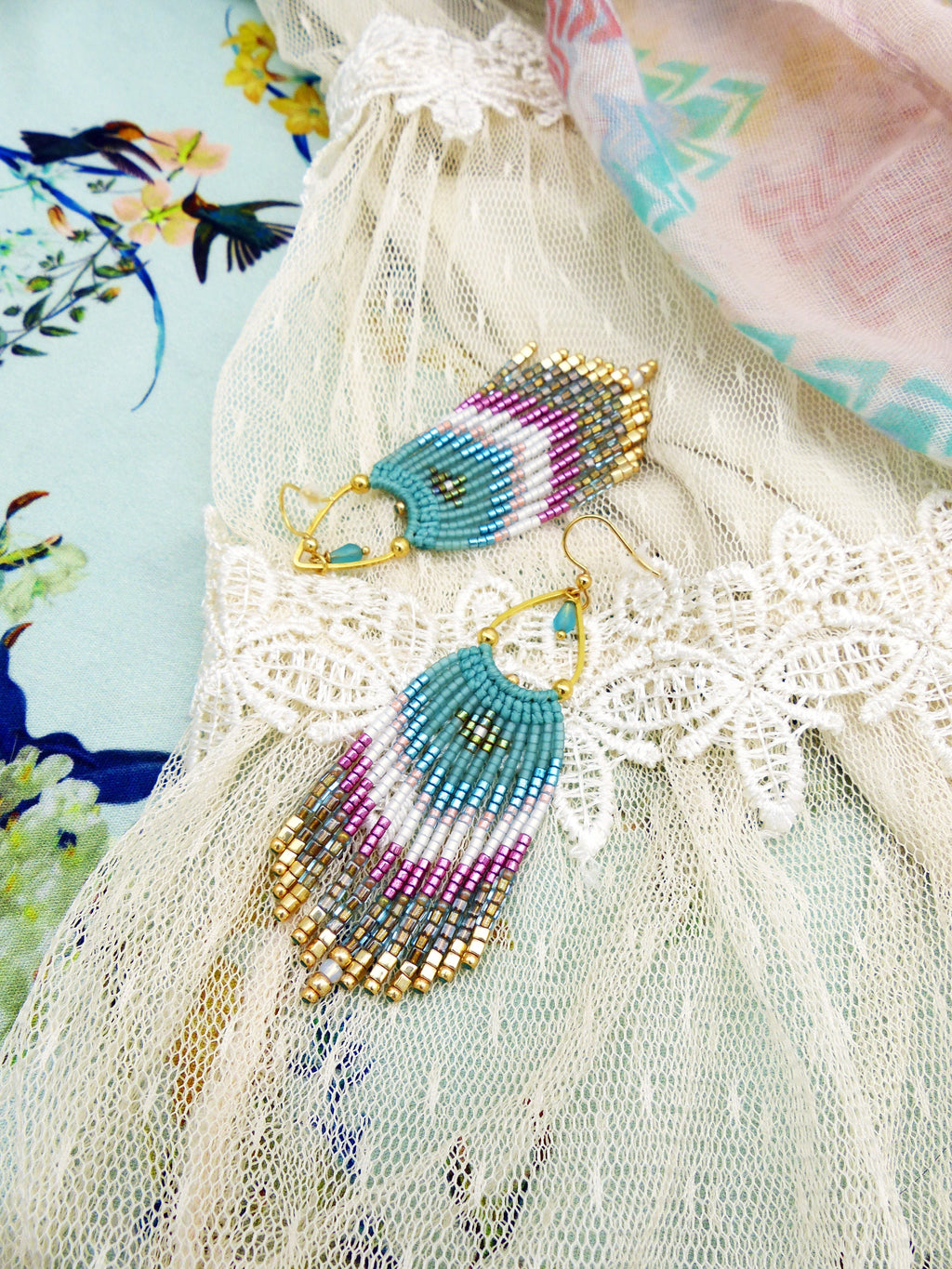 Peut inclure: Une paire de boucles d'oreilles en perles turquoise et dorées avec un design en frange. Les boucles d'oreilles sont suspendues à un tissu en dentelle blanche.