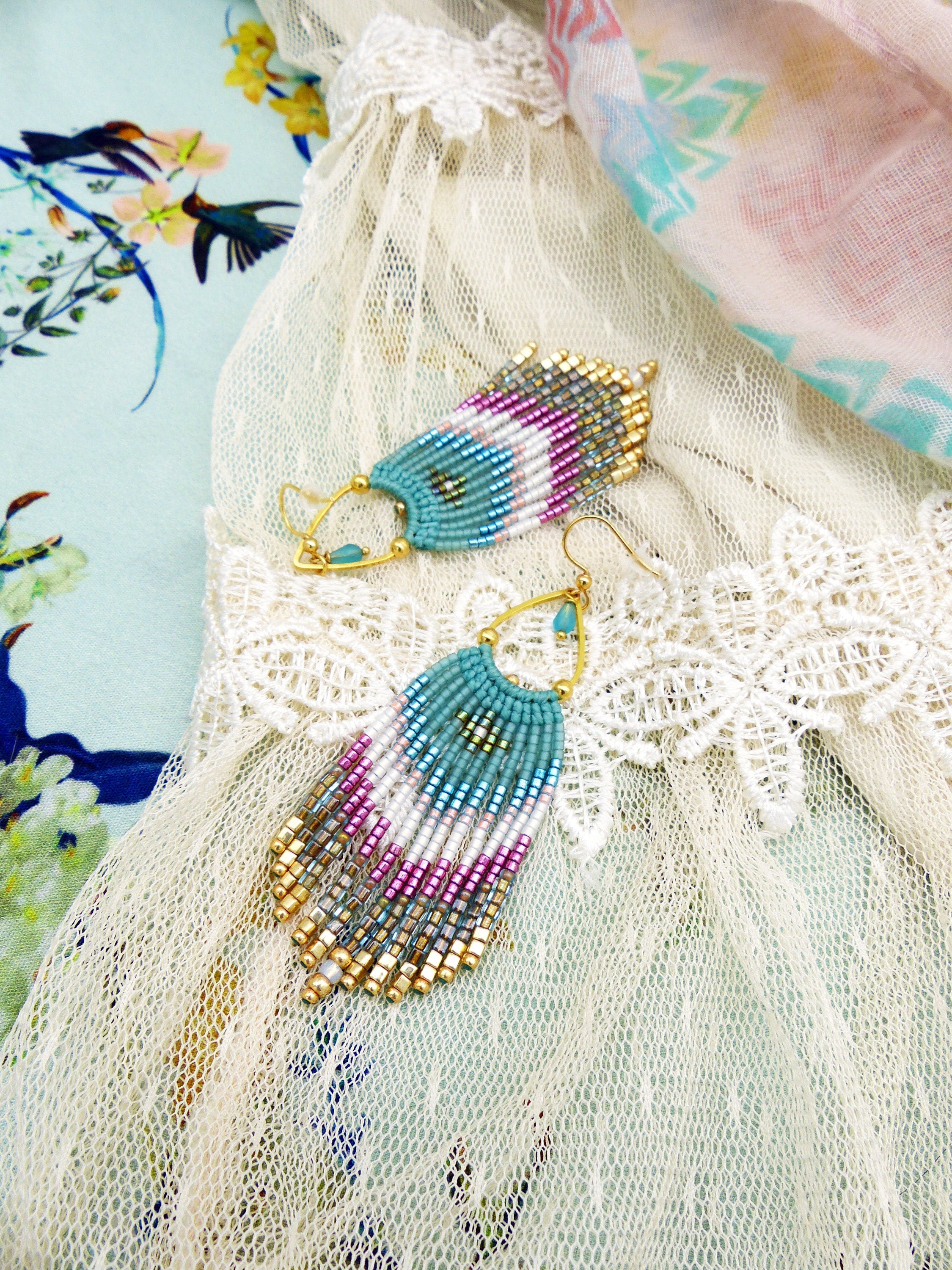 Peut inclure: Une paire de boucles d'oreilles en perles turquoise et dorées avec un design en frange. Les boucles d'oreilles sont suspendues à un tissu en dentelle blanche.