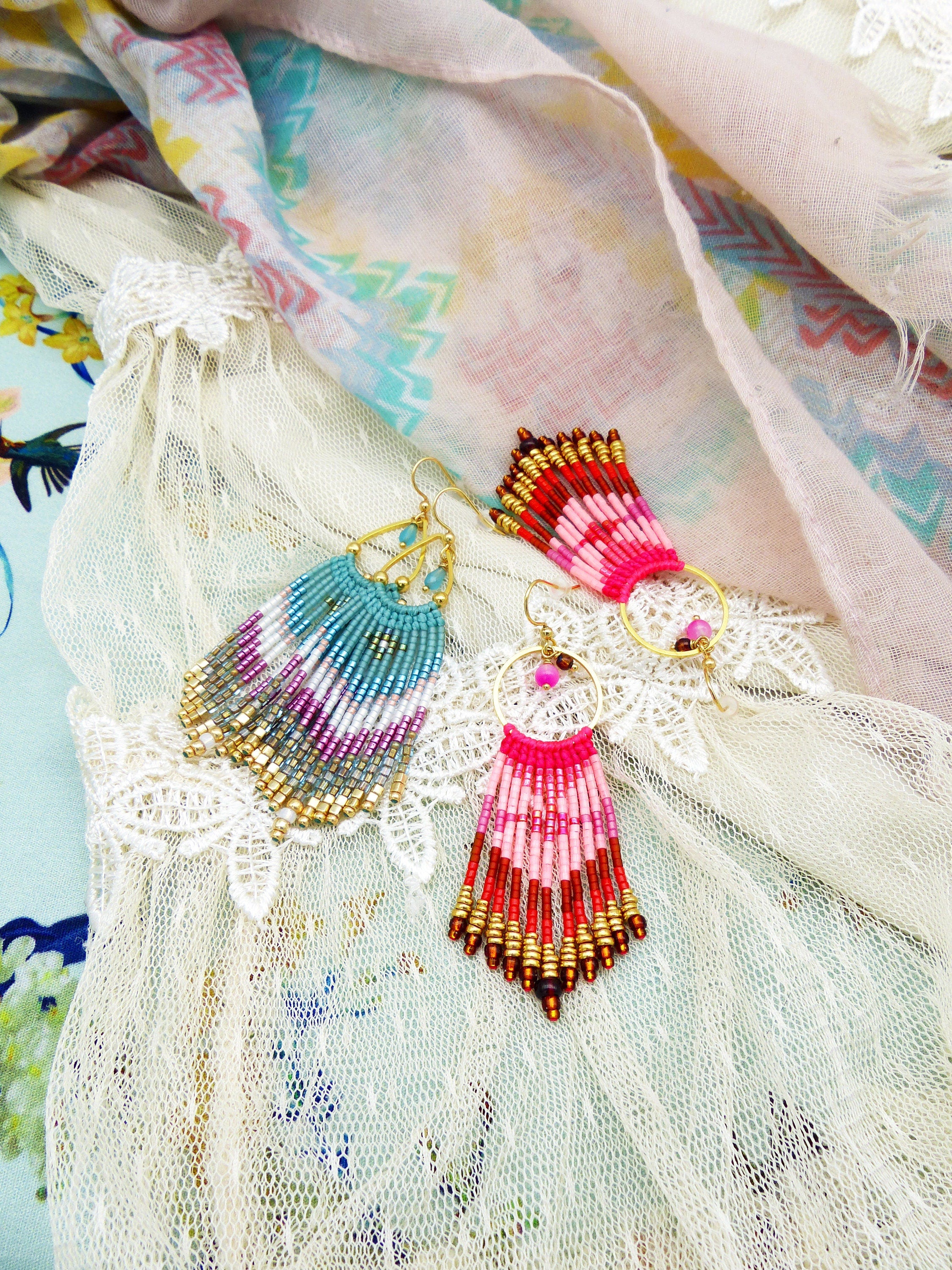 Peut inclure: Une paire de boucles d'oreilles en perles avec des accents dorés. Une boucle d'oreille est bleue, rose et blanche, et l'autre est rouge, rose et blanche.