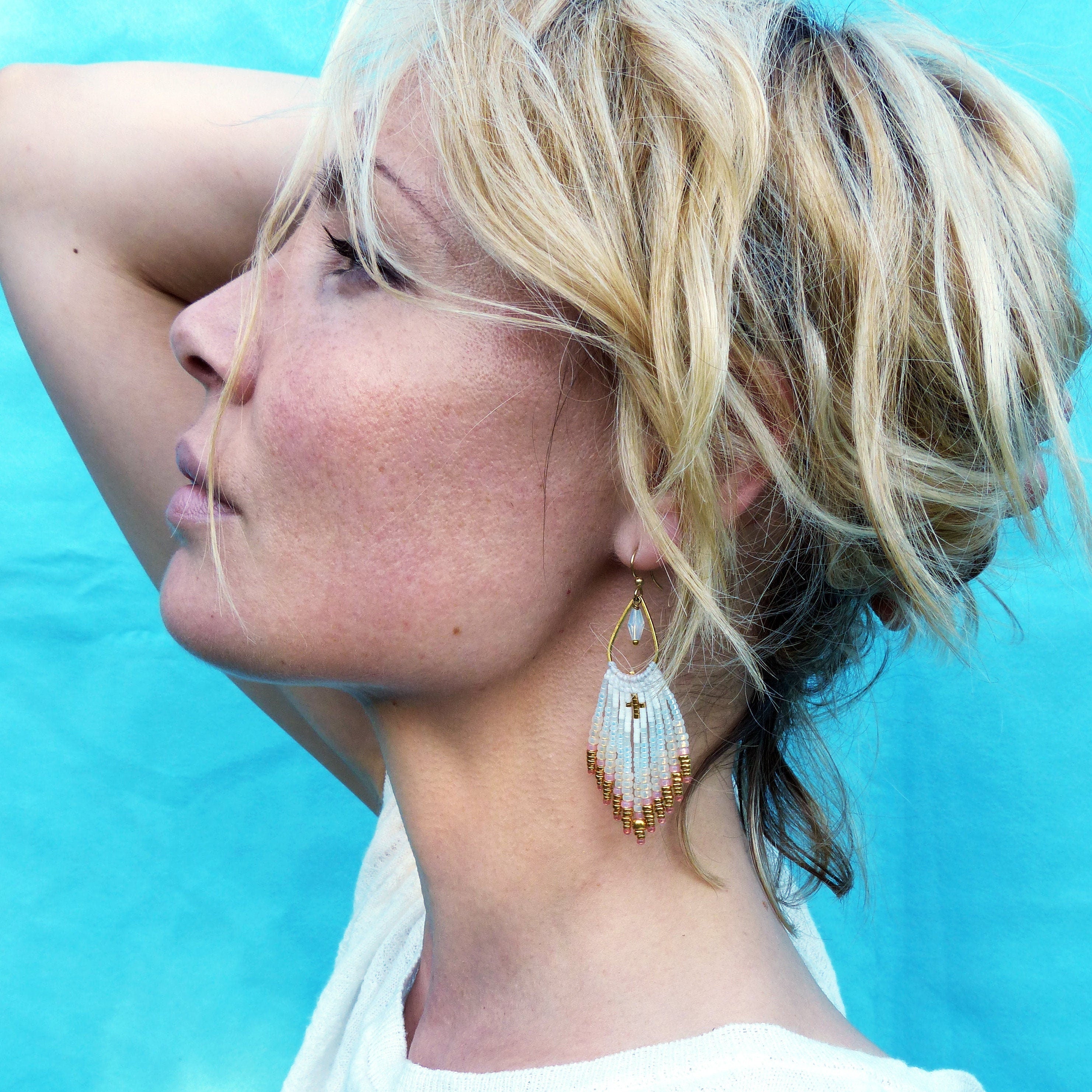 Peut inclure: Une paire de longues boucles d'oreilles en perles avec un pendentif en forme de croix dorée et un motif blanc, rose et or.
