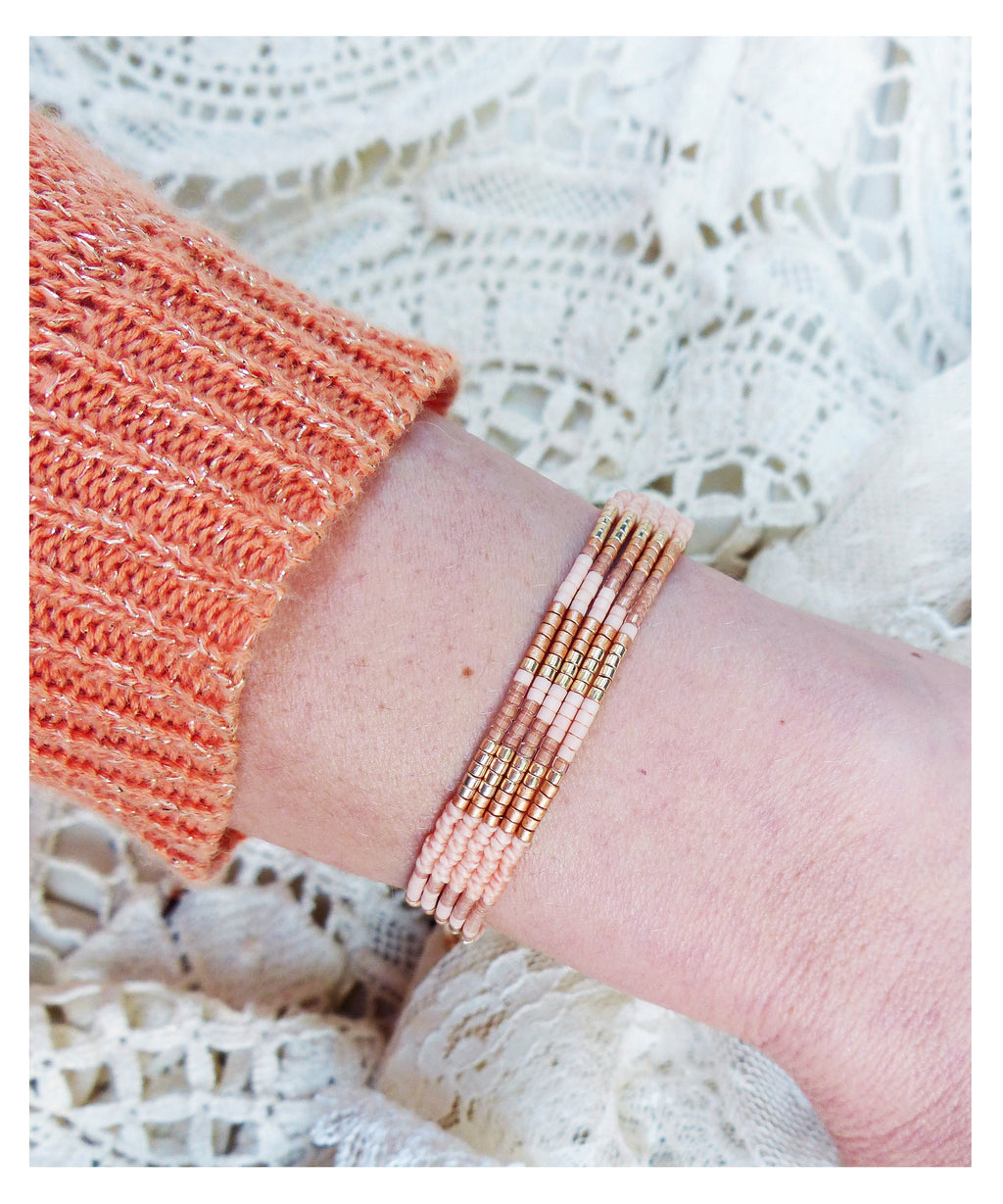 Peut inclure: Un bracelet superposé avec des perles roses et dorées. Le bracelet est composé de petites perles rondes enfilées dans un motif répétitif. Les perles sont de couleur rose clair avec des accents dorés.