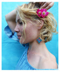 Peut inclure: Une femme aux cheveux blonds porte une fleur rose dans les cheveux, un haut bleu à épaules dénudées et des boucles d'oreilles en macramé colorées. Les boucles d'oreilles sont en forme de losange avec des fils bleus, rouges et oranges.