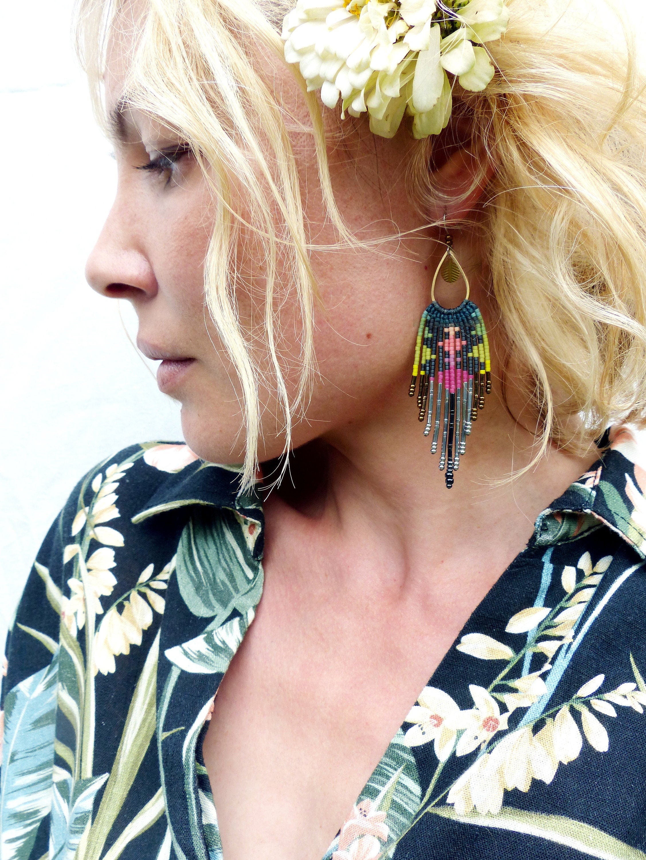 Peut inclure: Une femme portant une chemise à imprimé floral noir et vert avec une paire de longues boucles d'oreilles en perles. Les boucles d'oreilles sont faites de perles colorées et ont un design en forme de glands.