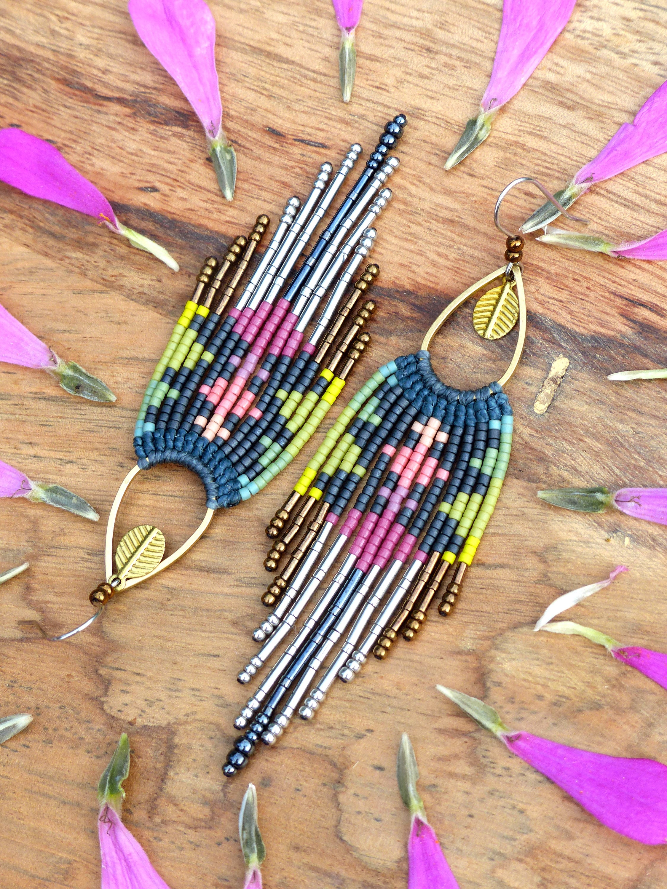 Peut inclure: Une paire de longues boucles d'oreilles en perles colorées avec un motif géométrique. Les boucles d'oreilles sont faites de perles argentées, dorées et noires, et elles ont un design en forme de glands. Les boucles d'oreilles sont suspendues à un crochet doré.