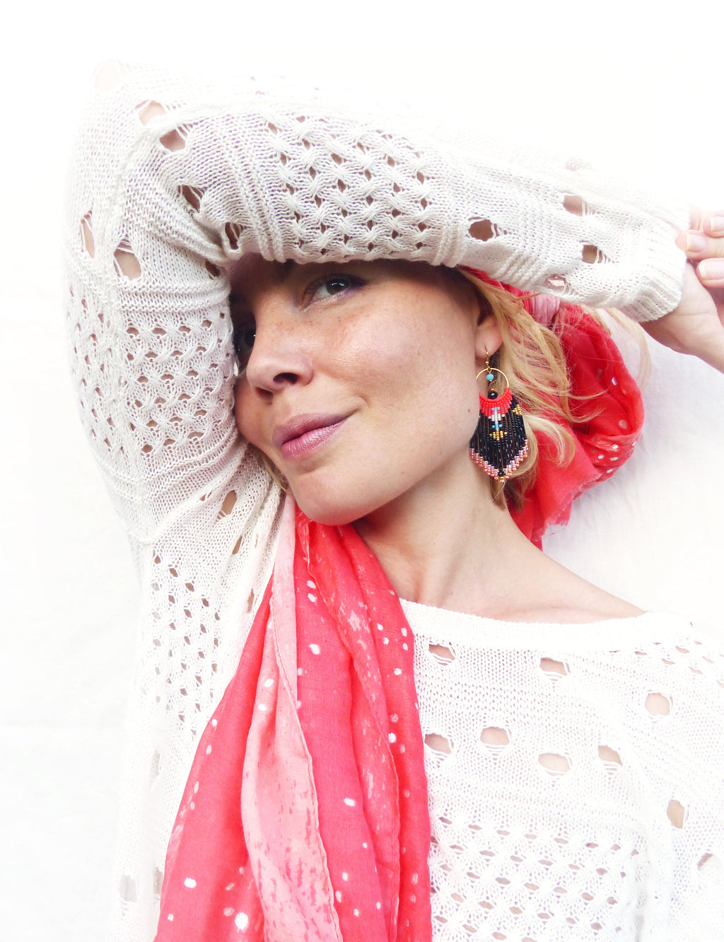 Peut inclure: Une femme portant un pull en crochet blanc avec une écharpe rose et blanche. Elle porte des boucles d'oreilles en perles noires et rouges avec des accents turquoise.