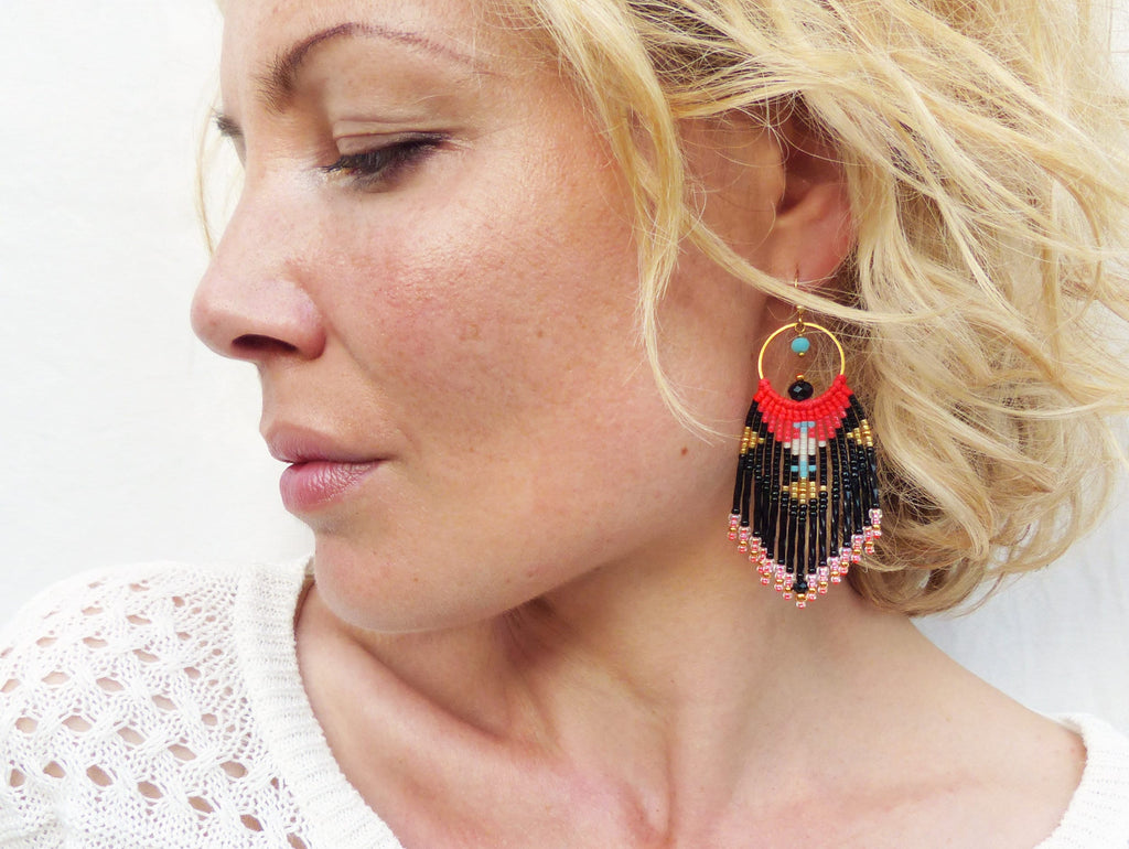 Peut inclure: Une paire de boucles d'oreilles pendantes avec une frange de perles noires, rouges et turquoise. Les boucles d'oreilles sont faites avec un anneau doré et ont un motif géométrique.