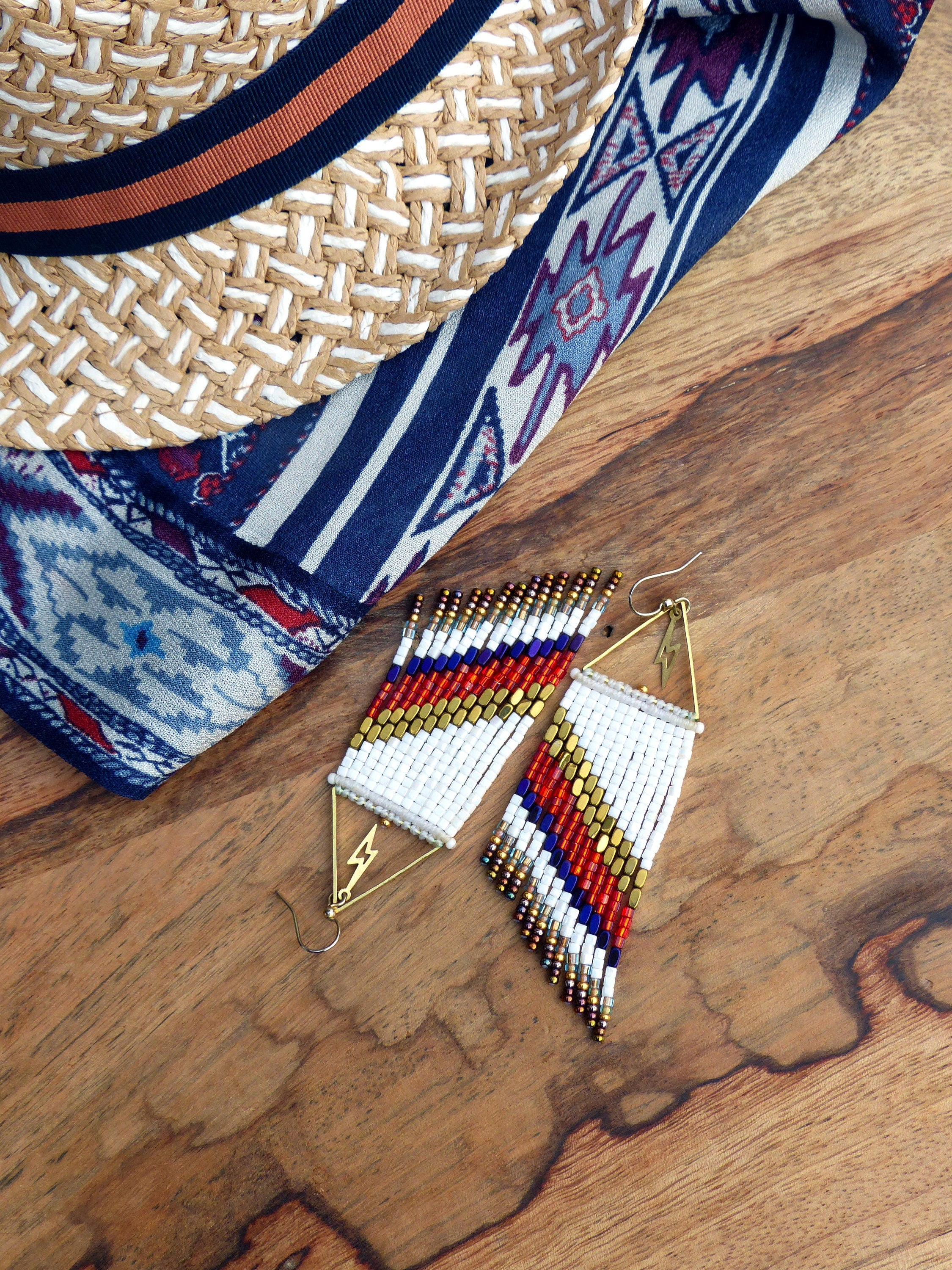 Peut inclure: Une paire de longues boucles d'oreilles en perles avec un motif blanc, rouge et bleu. Les boucles d'oreilles ont un motif d'éclair en haut et pendent jusqu'à environ 15 cm de long.