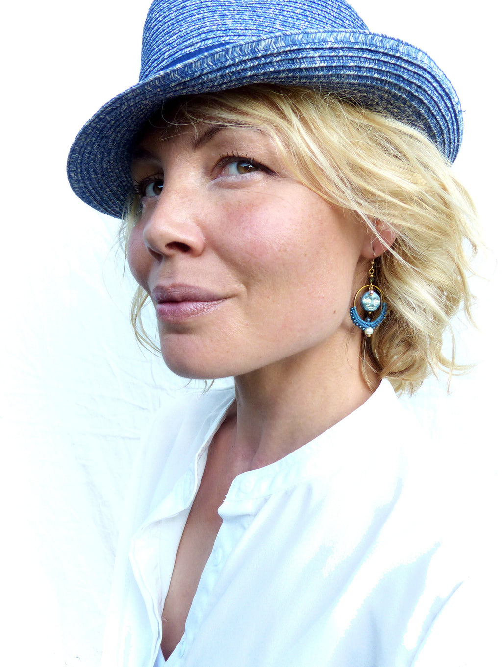 Peut inclure: Une femme portant un chapeau de paille bleu et une chemise blanche à col avec une boucle d'oreille en perles bleues et dorées.