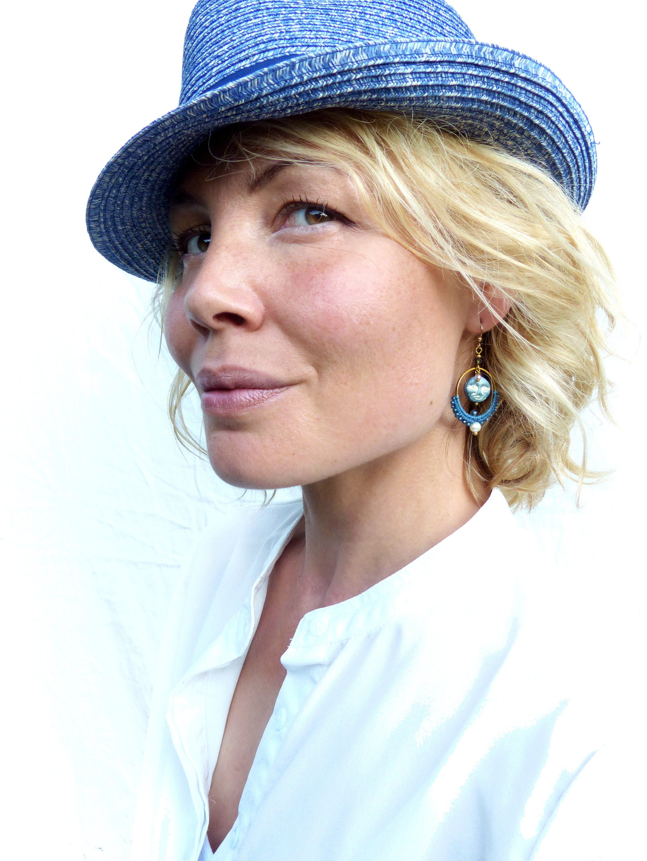 Peut inclure: Une femme portant un chapeau de paille bleu et une chemise blanche à col avec une boucle d'oreille en perles bleues et dorées.