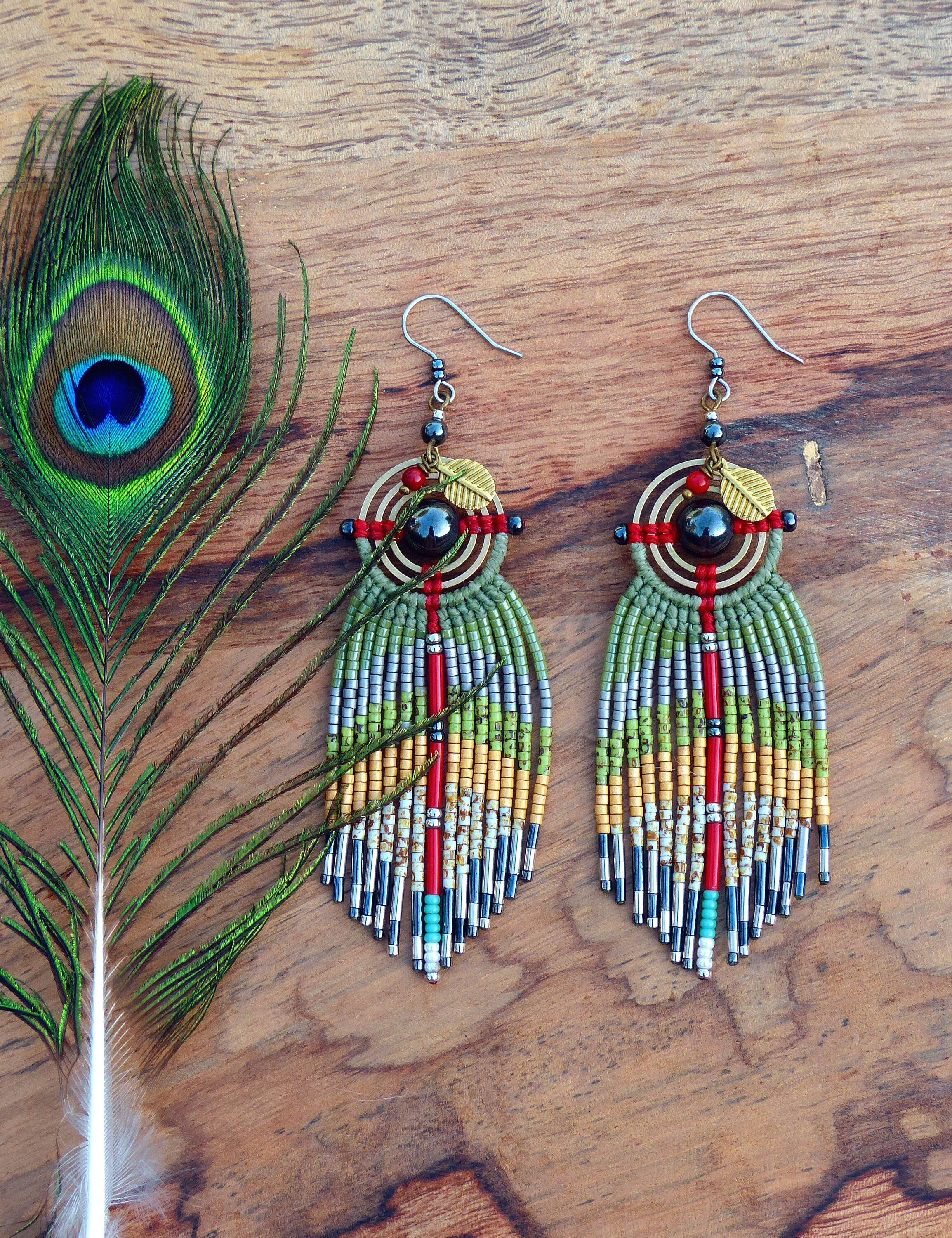 Peut inclure: Une paire de boucles d'oreilles en perles vertes, rouges et dorées avec des accents de pierre noire et de feuilles dorées. Les boucles d'oreilles sont suspendues à des crochets argentés.