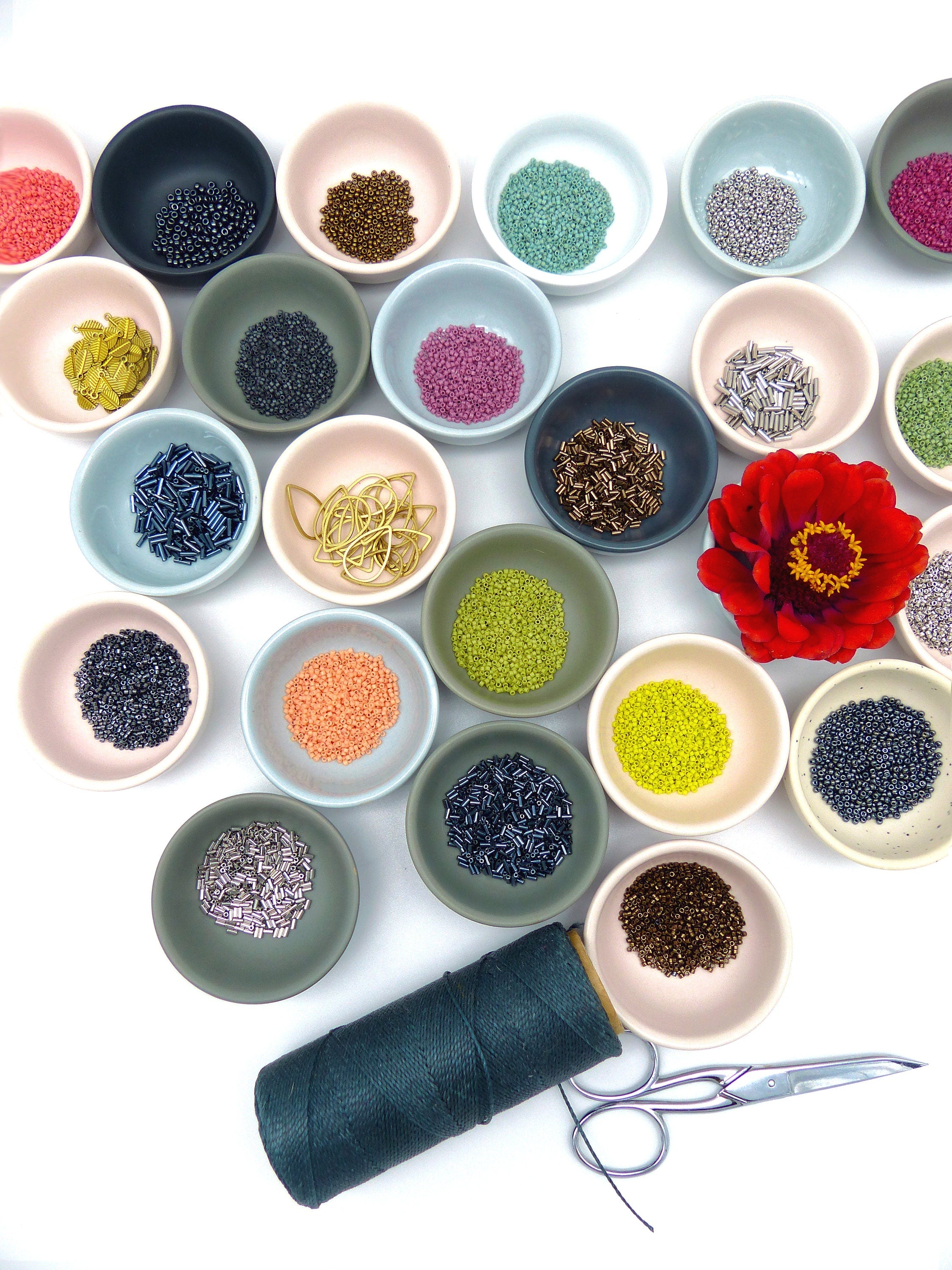 Peut inclure: Assortiment de perles et de trouvailles dans de petits bols, y compris des perles dorées, argentées, noires, brunes, vertes et roses, ainsi que des trouvailles dorées et argentées. Une bobine de fil vert foncé et une paire de ciseaux argentés sont également inclus.