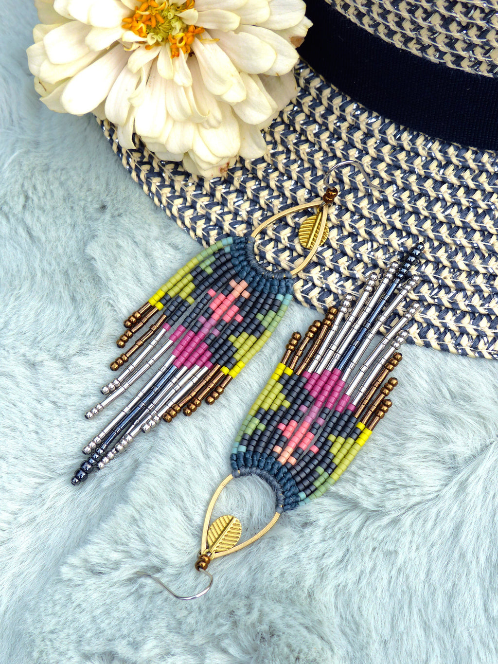 Peut inclure: Une paire de boucles d'oreilles en perles colorées avec un charme en feuille d'or. Les boucles d'oreilles sont faites avec une variété de perles, y compris l'argent, le brun, le rose, le bleu et le vert. Les boucles d'oreilles sont suspendues à un crochet en or.