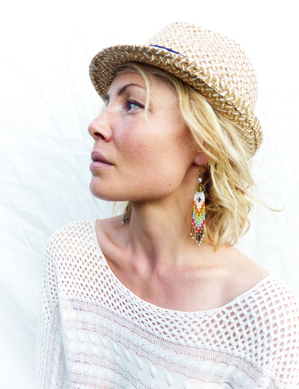 Peut inclure: Une femme portant un haut en crochet blanc et un fedora en paille avec un bandeau bleu. Elle porte des boucles d'oreilles en perles colorées.