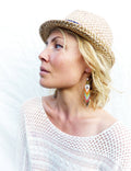 Peut inclure: Une femme portant un haut en crochet blanc et un fedora en paille avec un bandeau bleu. Elle porte des boucles d'oreilles en perles colorées.